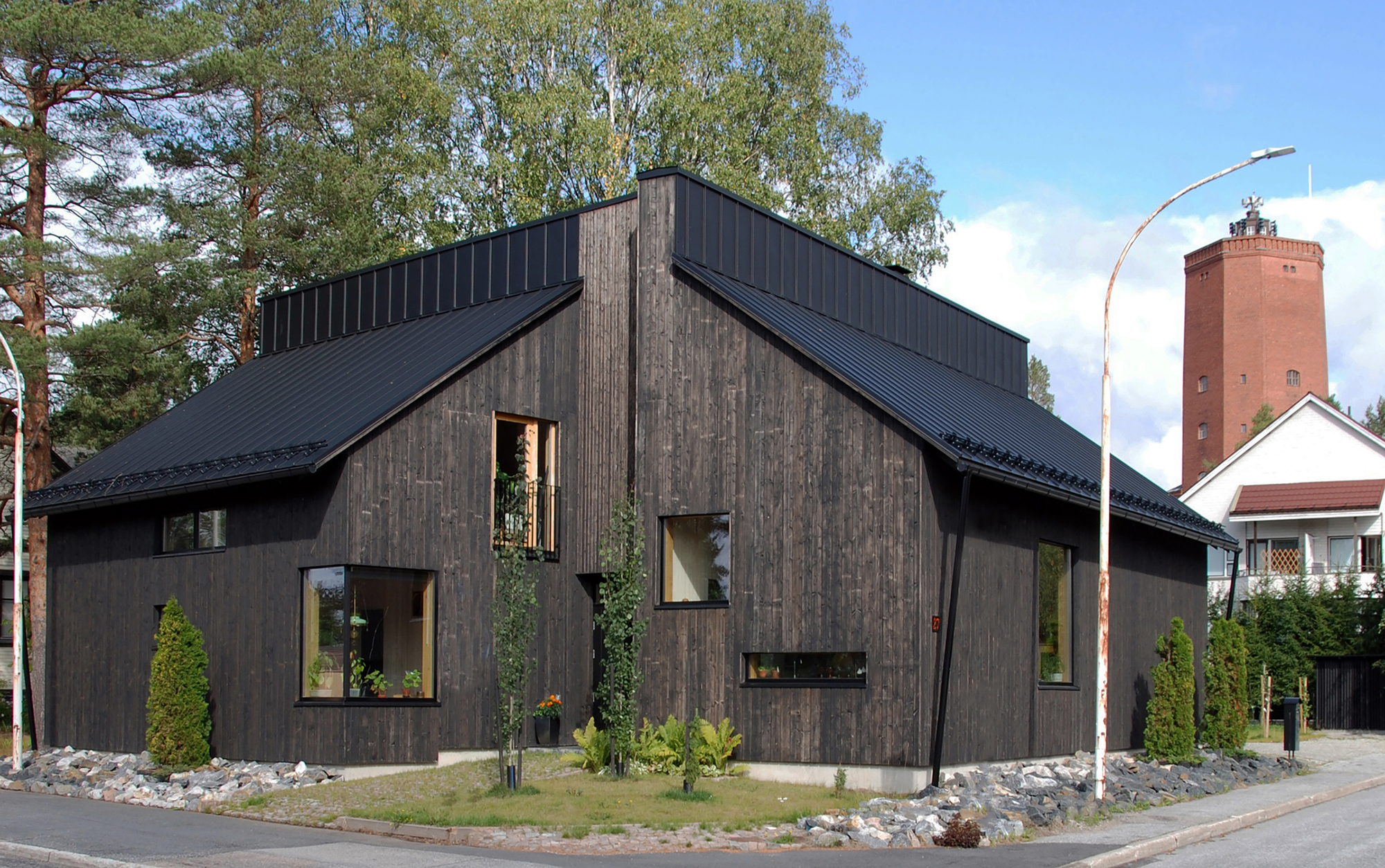 Street facade of black timber-clad volumes with gabled metal roof and scattered window openings