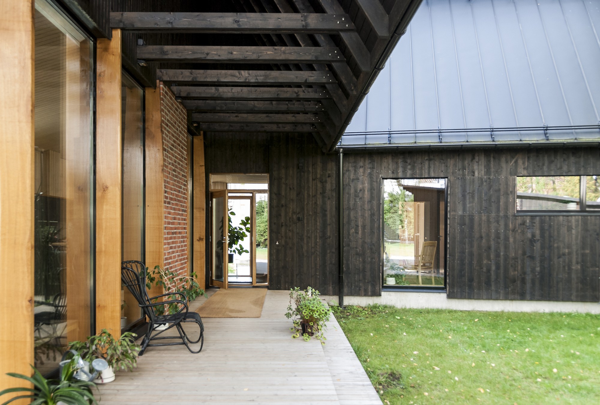 Covered walkway with exposed black-stained timber beams linking charred wood and brick volumes