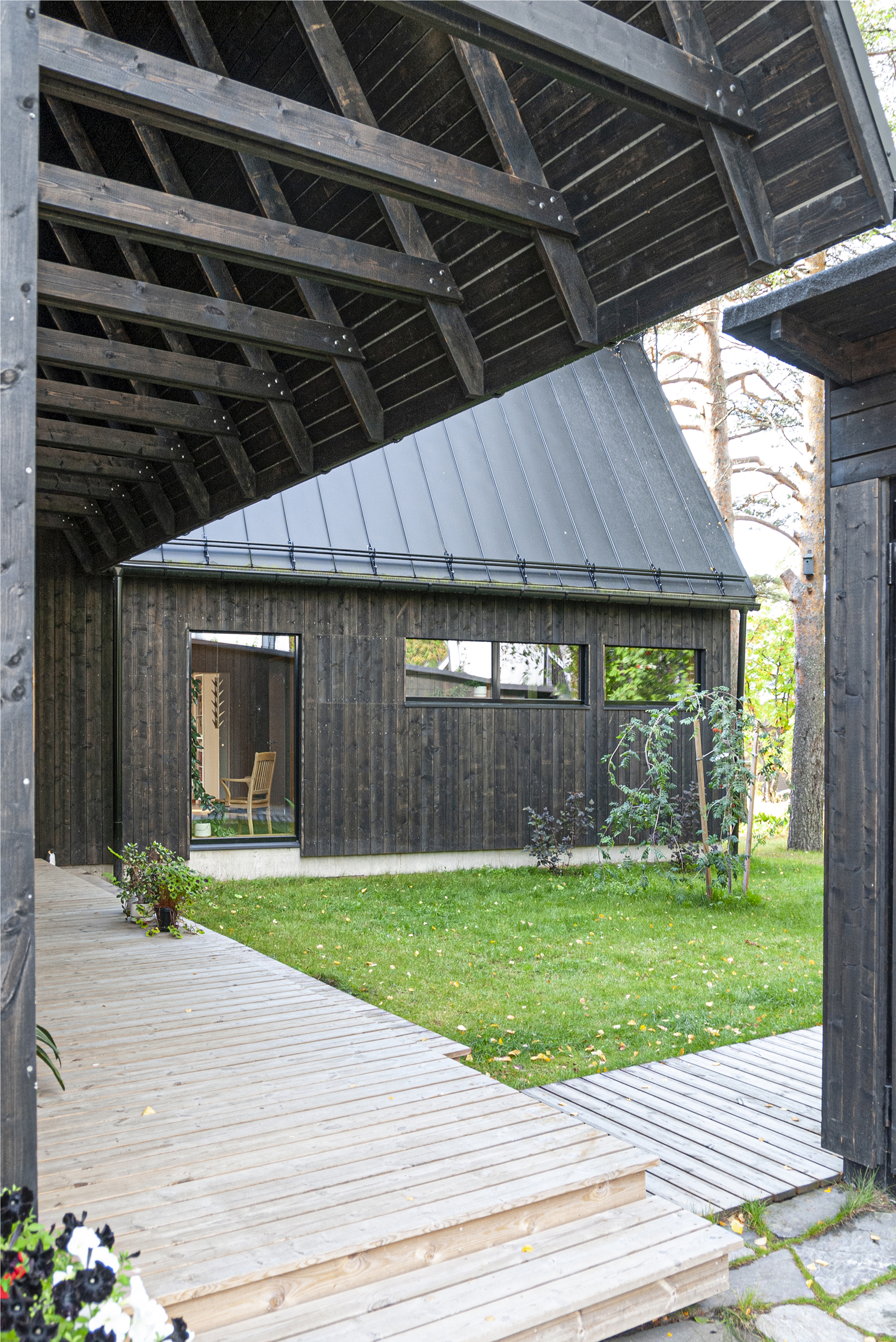 View from covered timber walkway through to charred wood pavilion across lawn courtyard in dappled sunlight