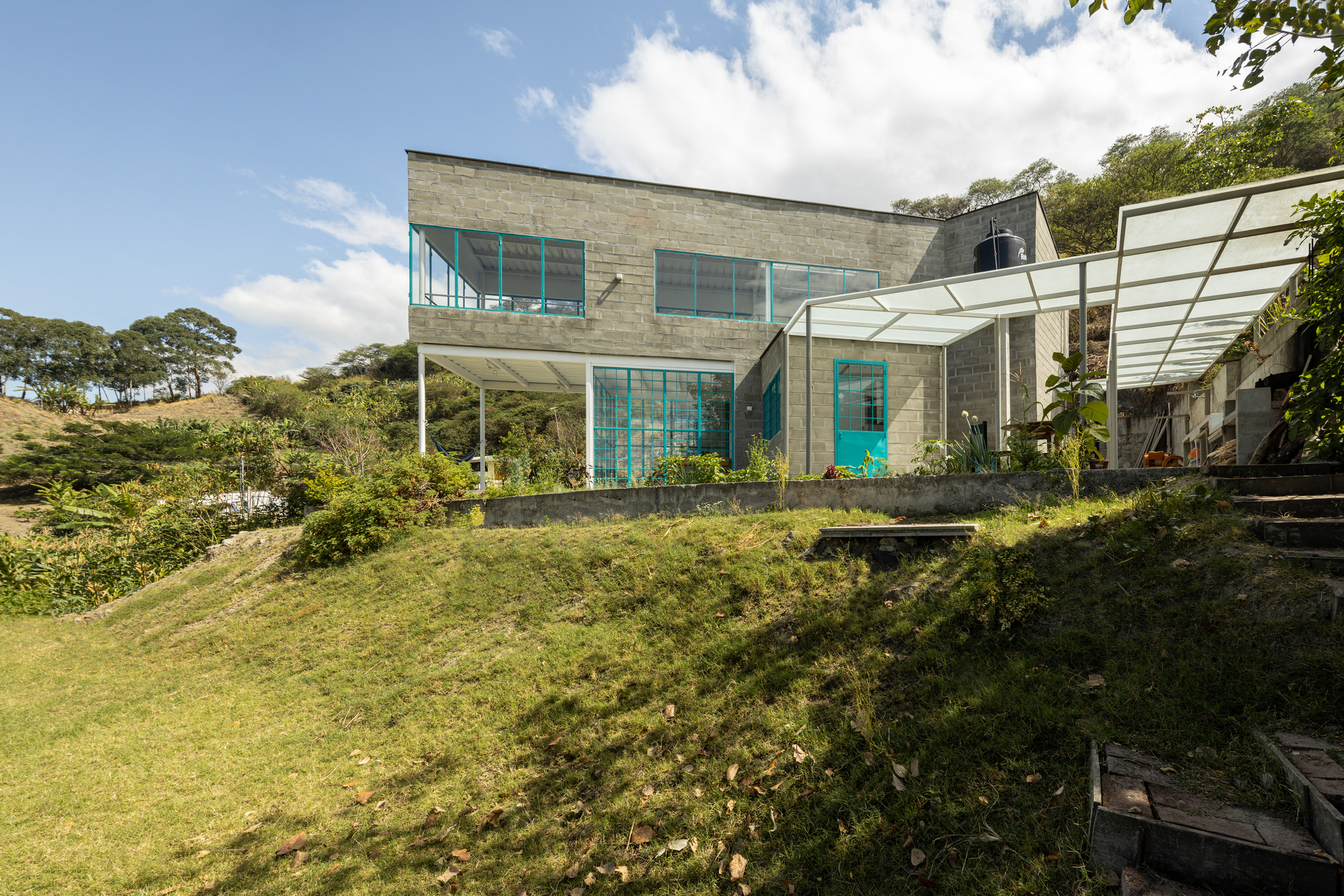 Rear facade with turquoise glazing set into concrete blockwork above a sloping lawn