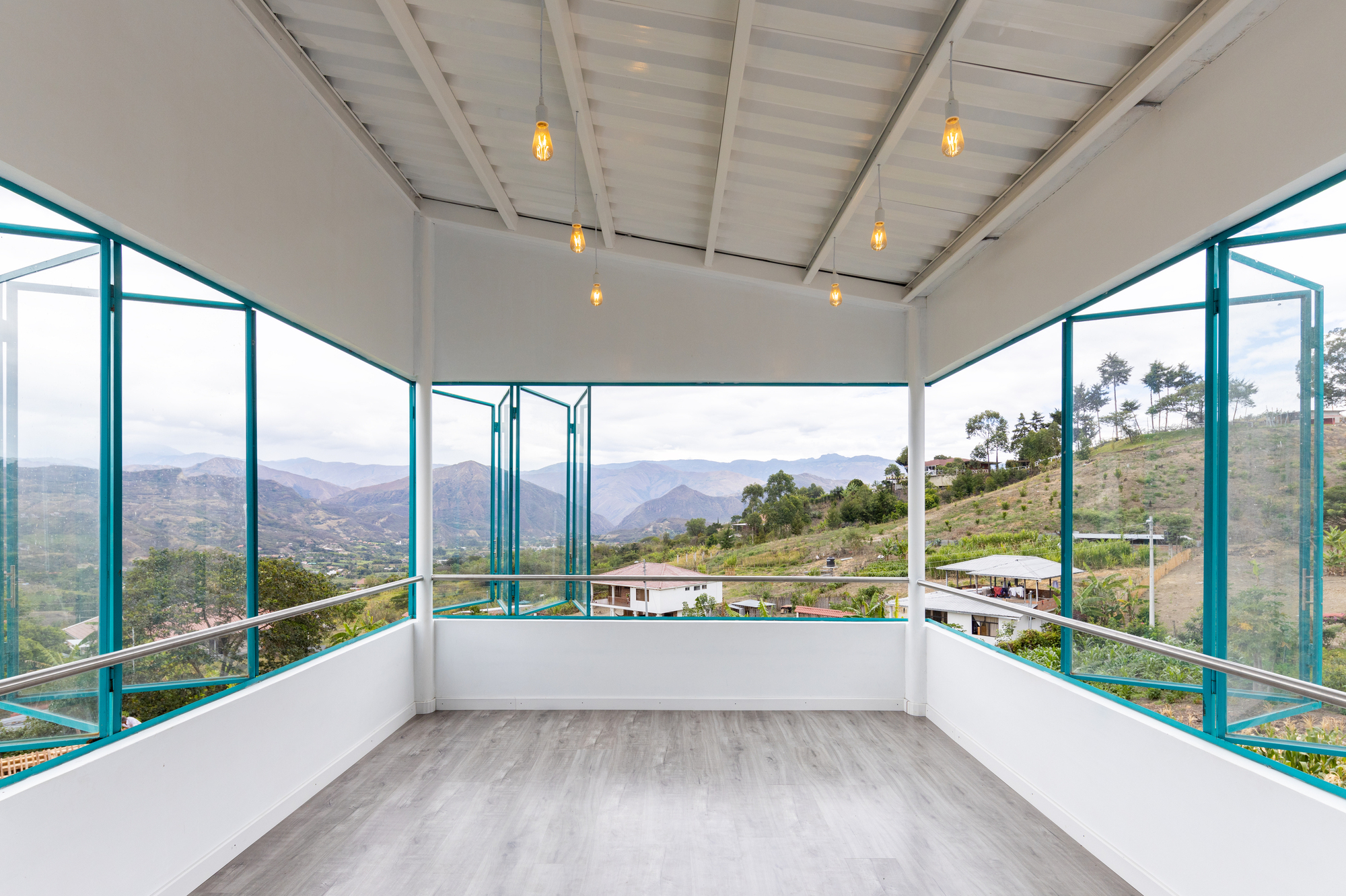 Upper-level room with exposed ceiling beams and full-height turquoise windows opening to hillside views
