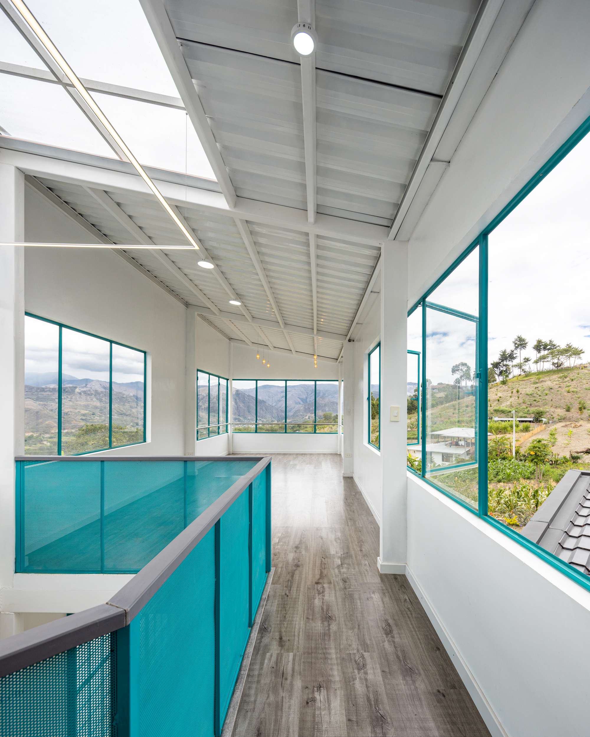 Upper level corridor with turquoise glass balustrade and floor-to-ceiling windows framing mountain views