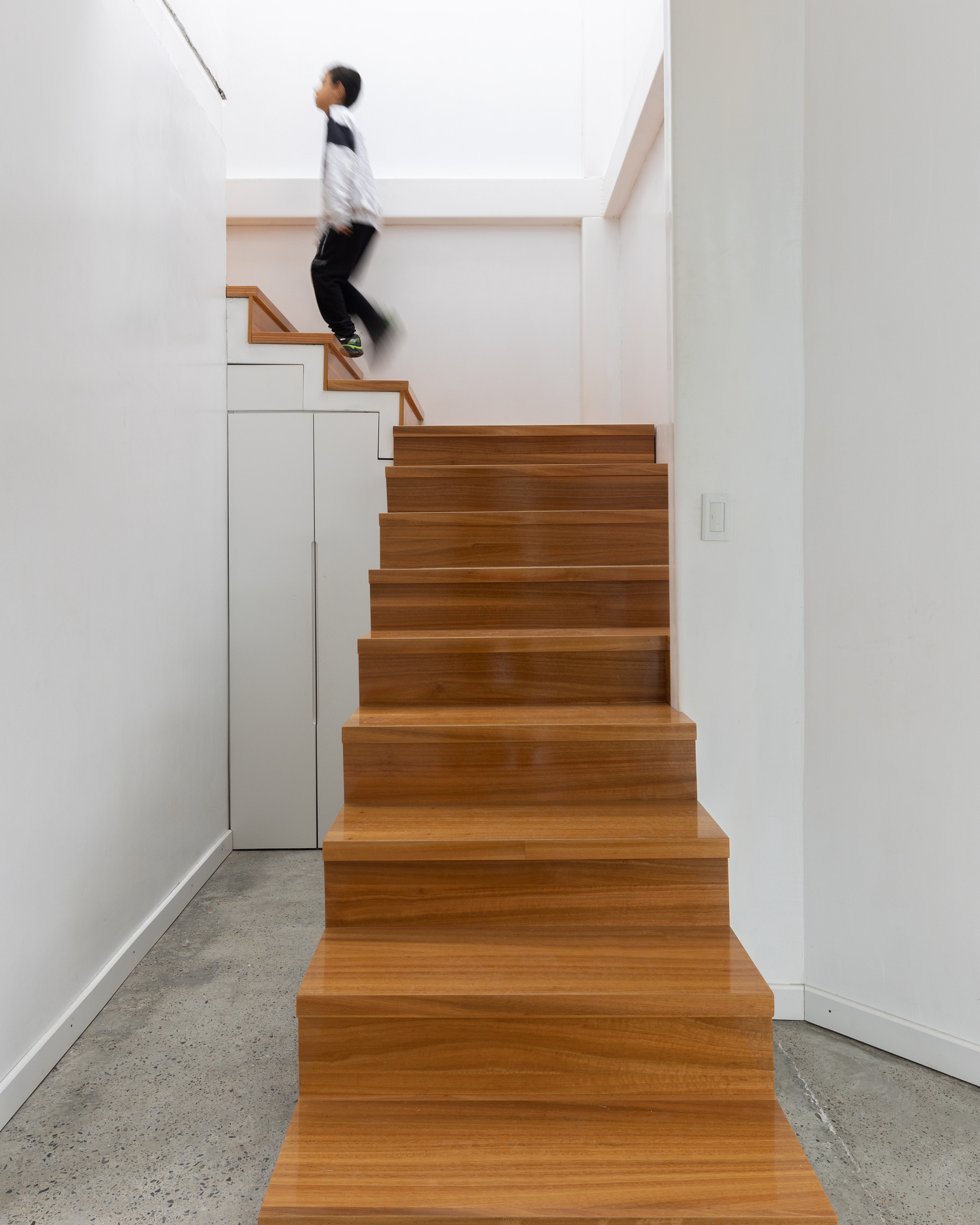 Warm wood stair treads meeting polished concrete flooring with a figure in motion overhead