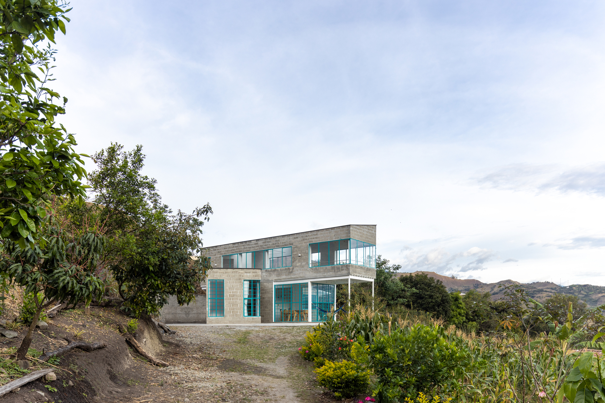 Two-story residence with concrete walls and glass facades on a hillside amid scattered vegetation