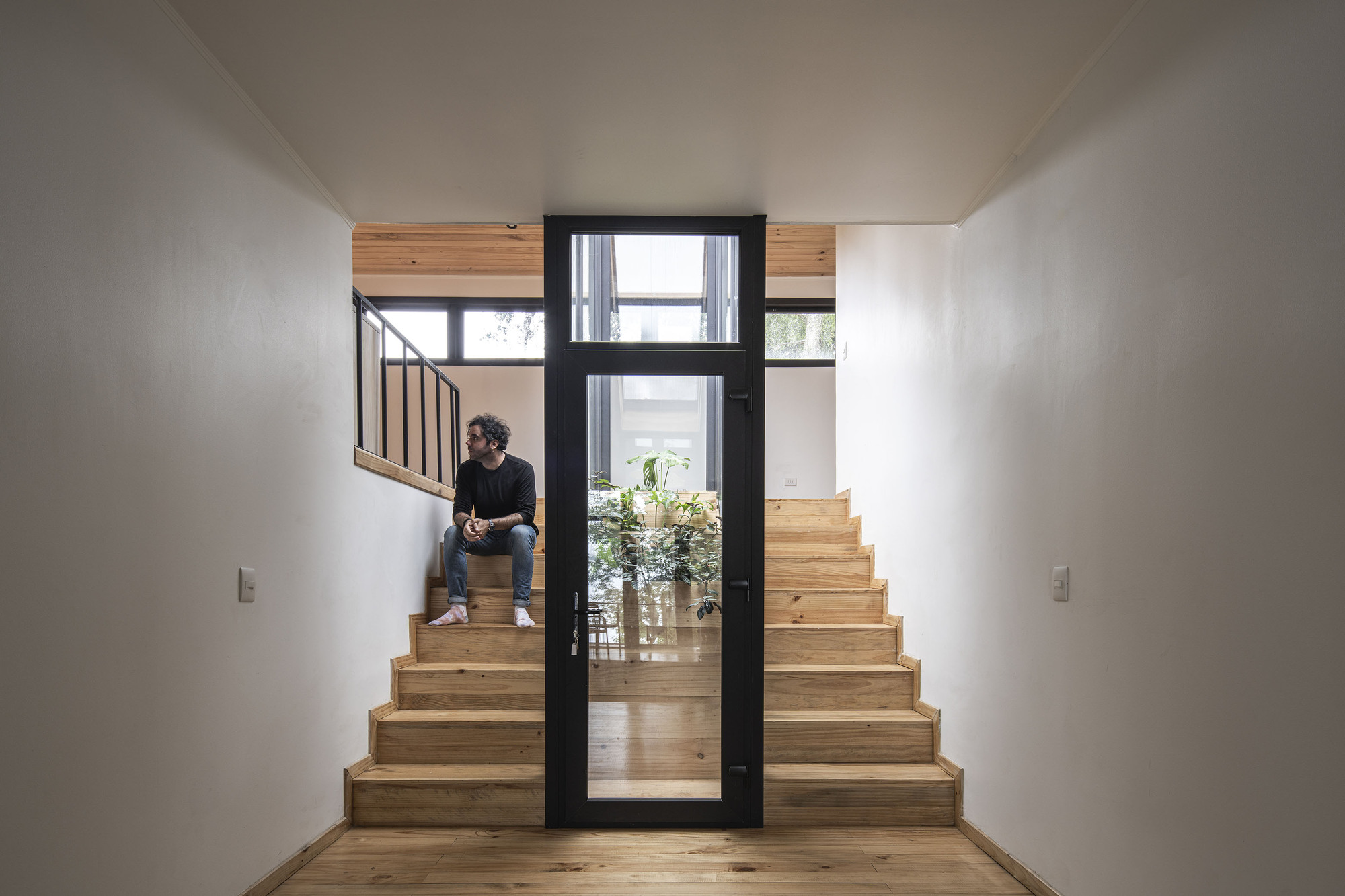 Timber staircase with a person seated midway and glazed door opening to planted courtyard beyond