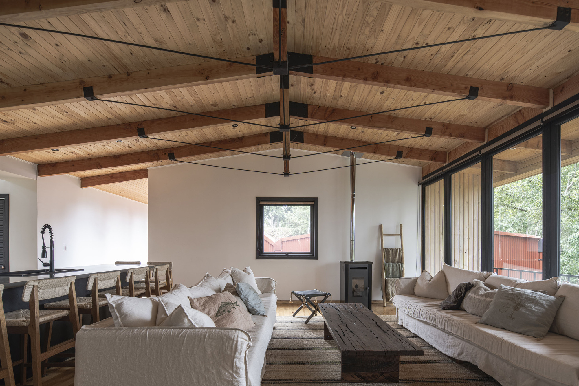 Open living space with exposed timber beams and planked ceiling above white walls and corner glazing
