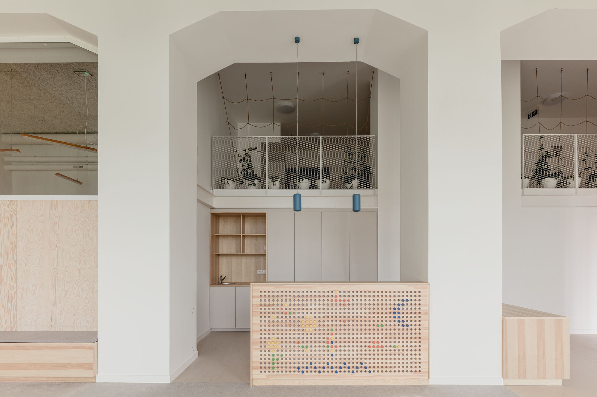 Reception counter with pegboard facade and colorful pegs beneath an arched opening and mezzanine with mesh balustrade