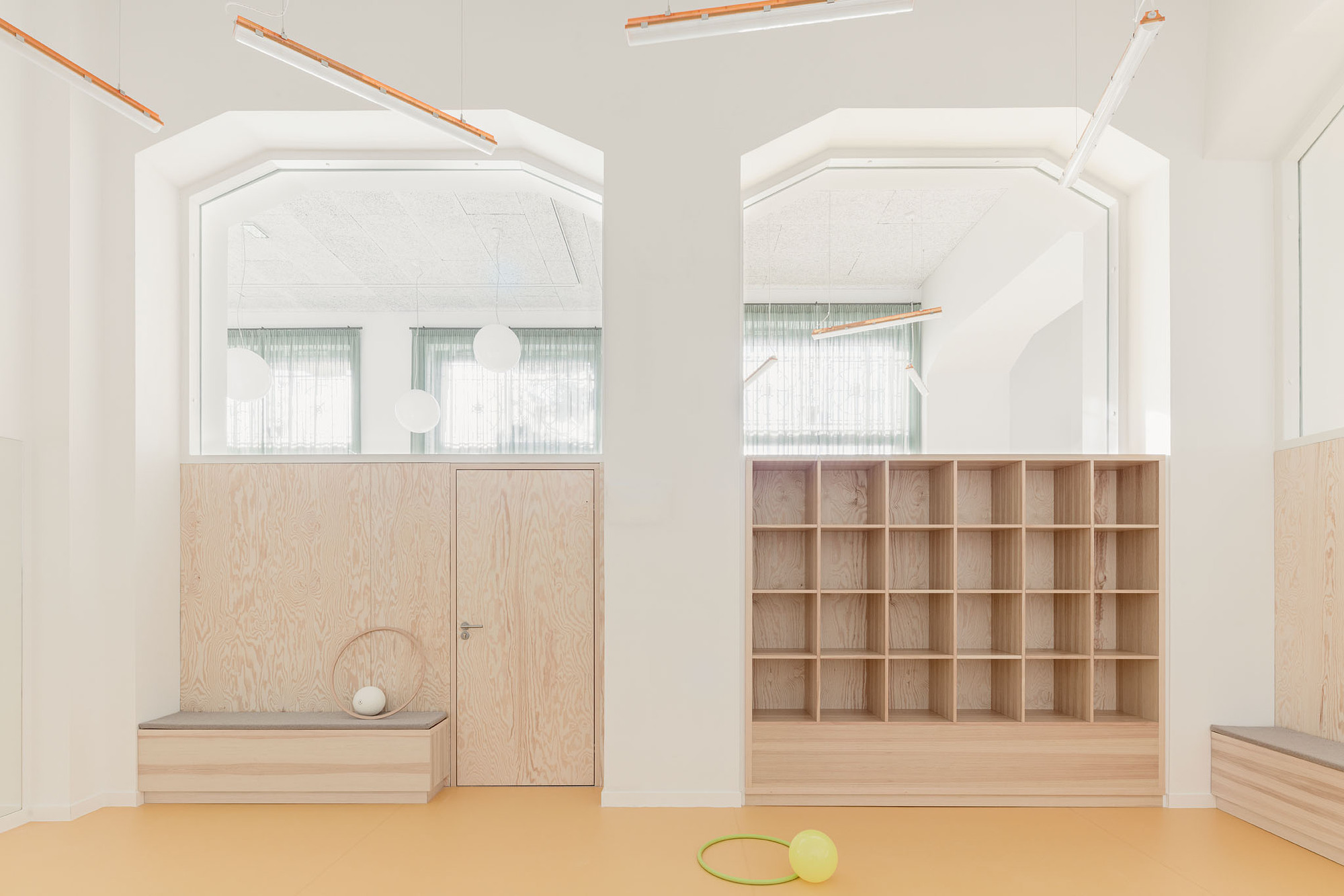 Interior room with arched white portals framing plywood doors and cubby shelving with orange linear lighting above