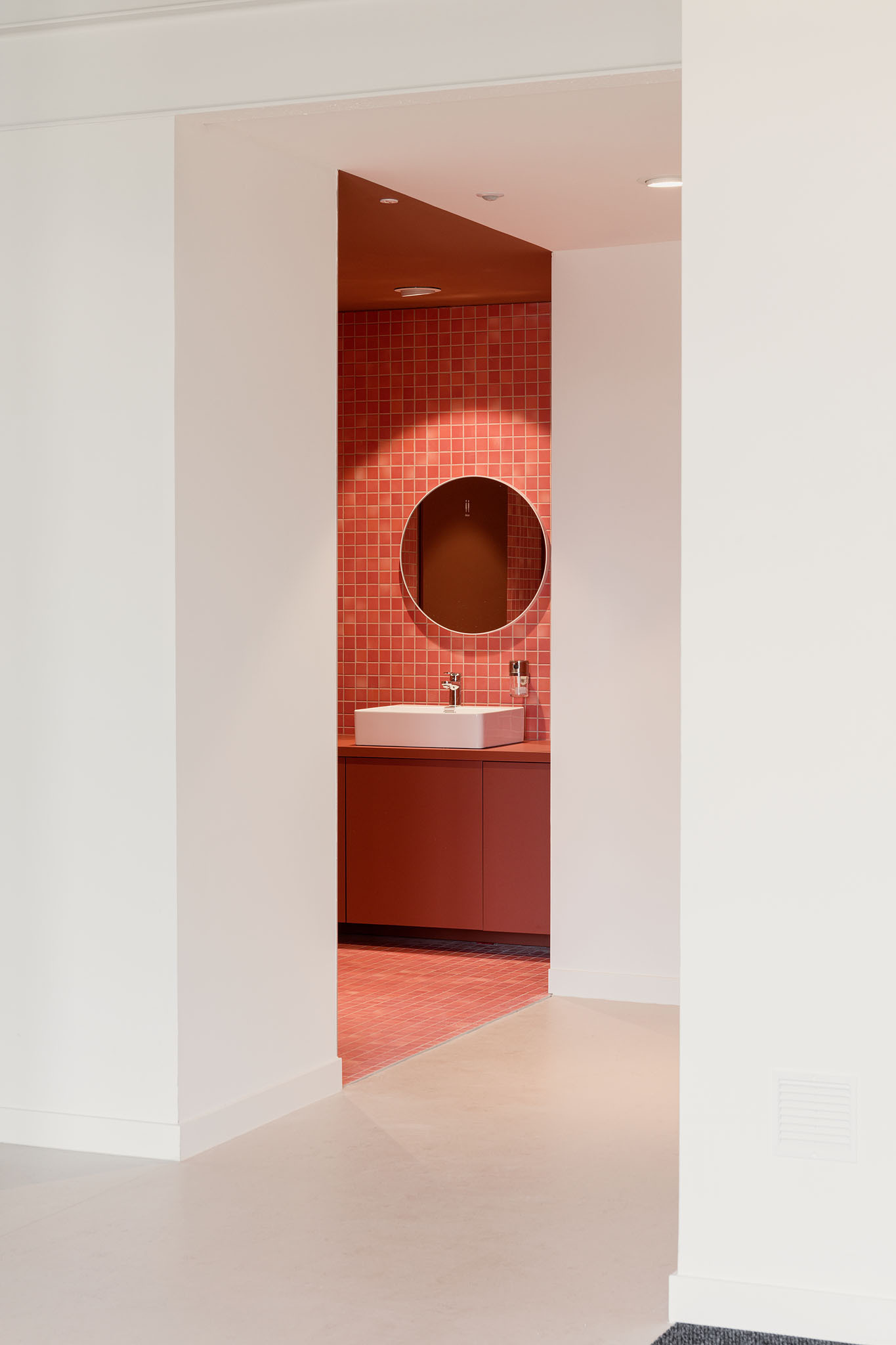 Doorway framing a terracotta-tiled bathroom alcove with circular mirror and white vessel sink