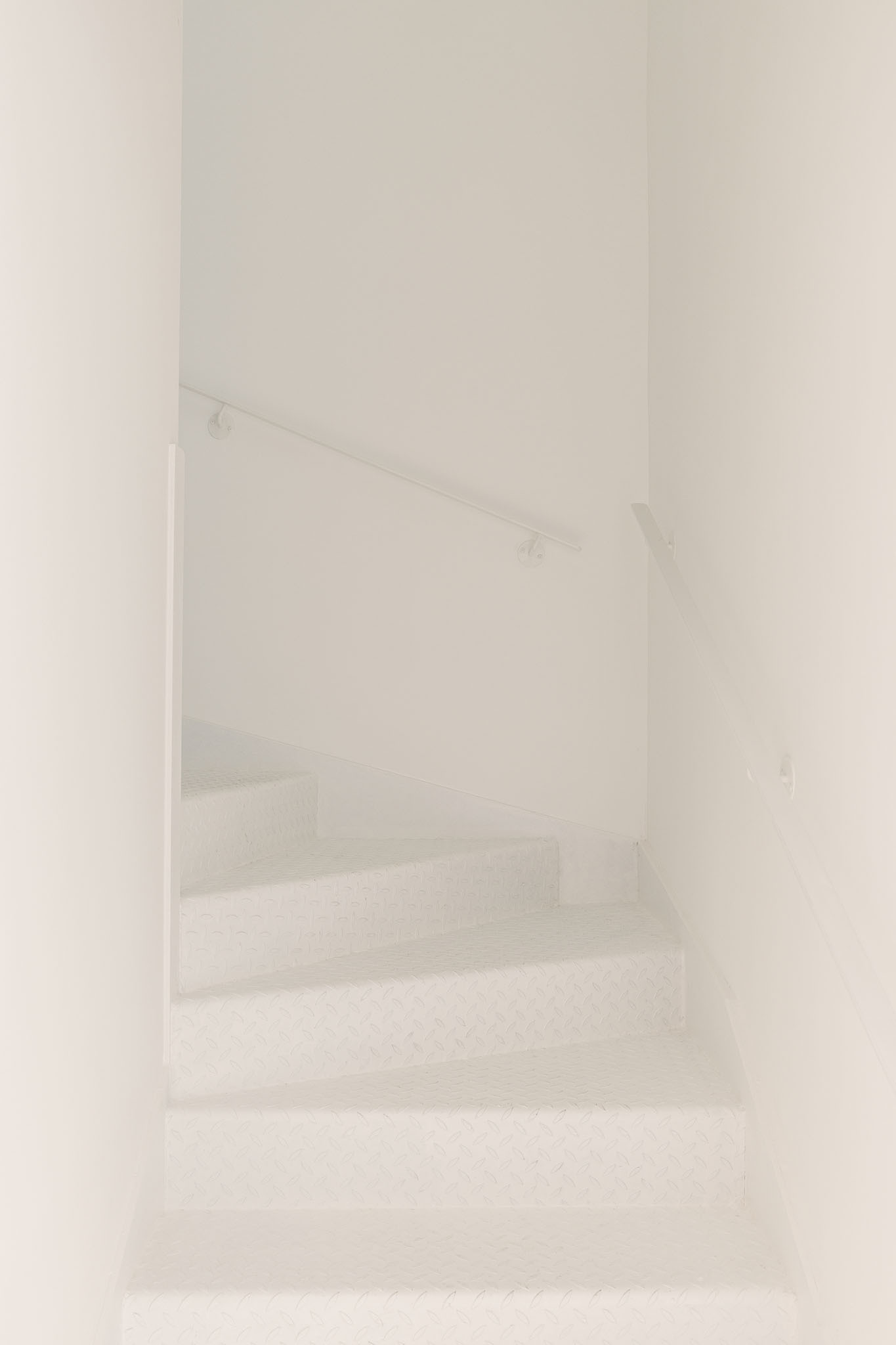 White plastered staircase with thin metal handrail ascending through a narrow enclosed stairwell
