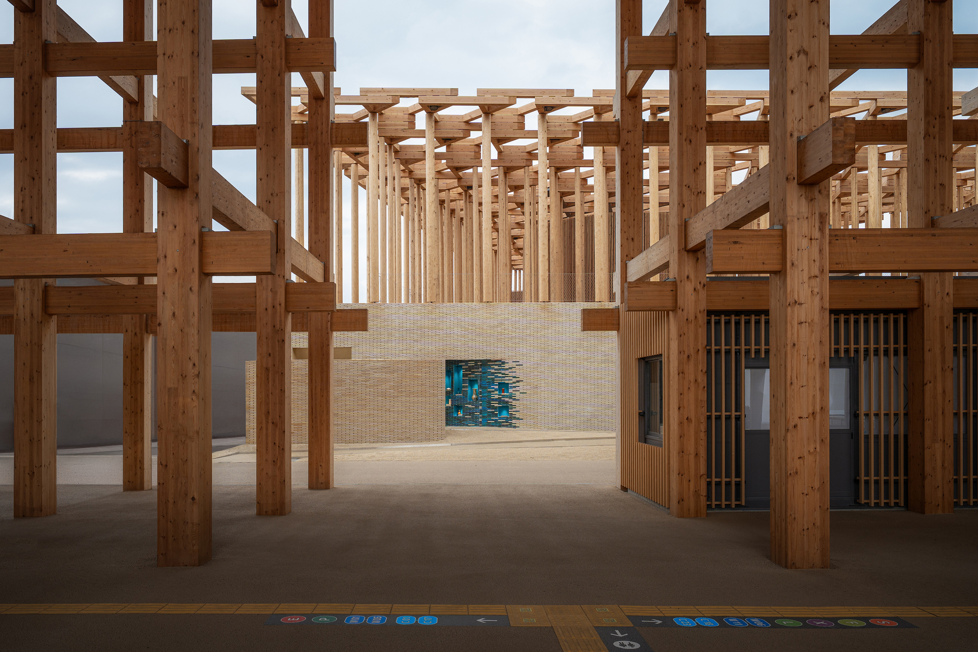 Interior view through timber post-and-beam structure with a blue glazed tile installation in the beige brick wall