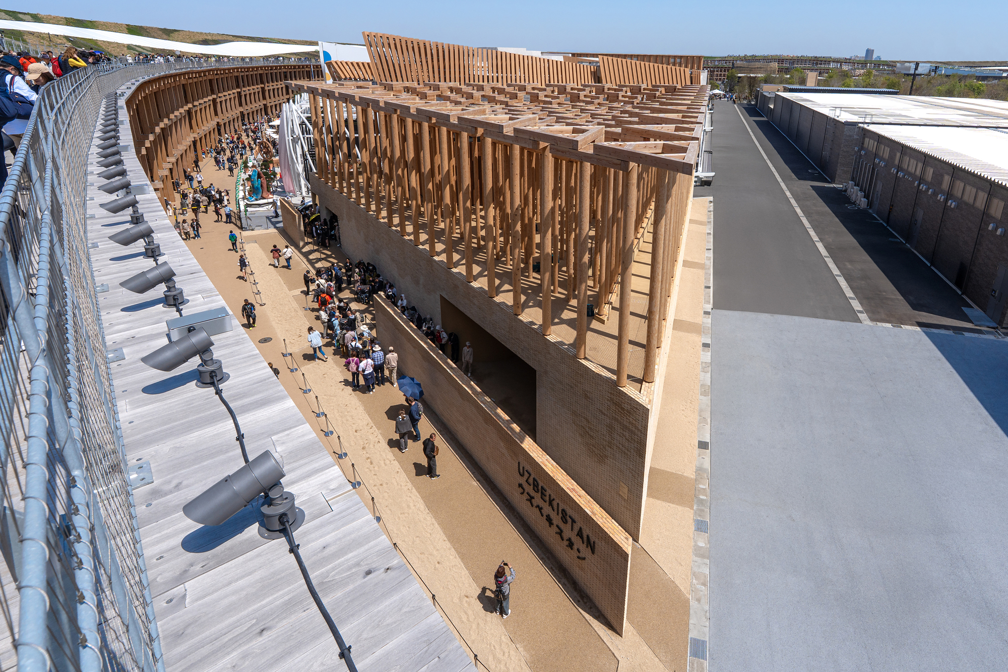 Aerial view of pavilion with diagonal timber roof structure and visitors gathered in the courtyard below