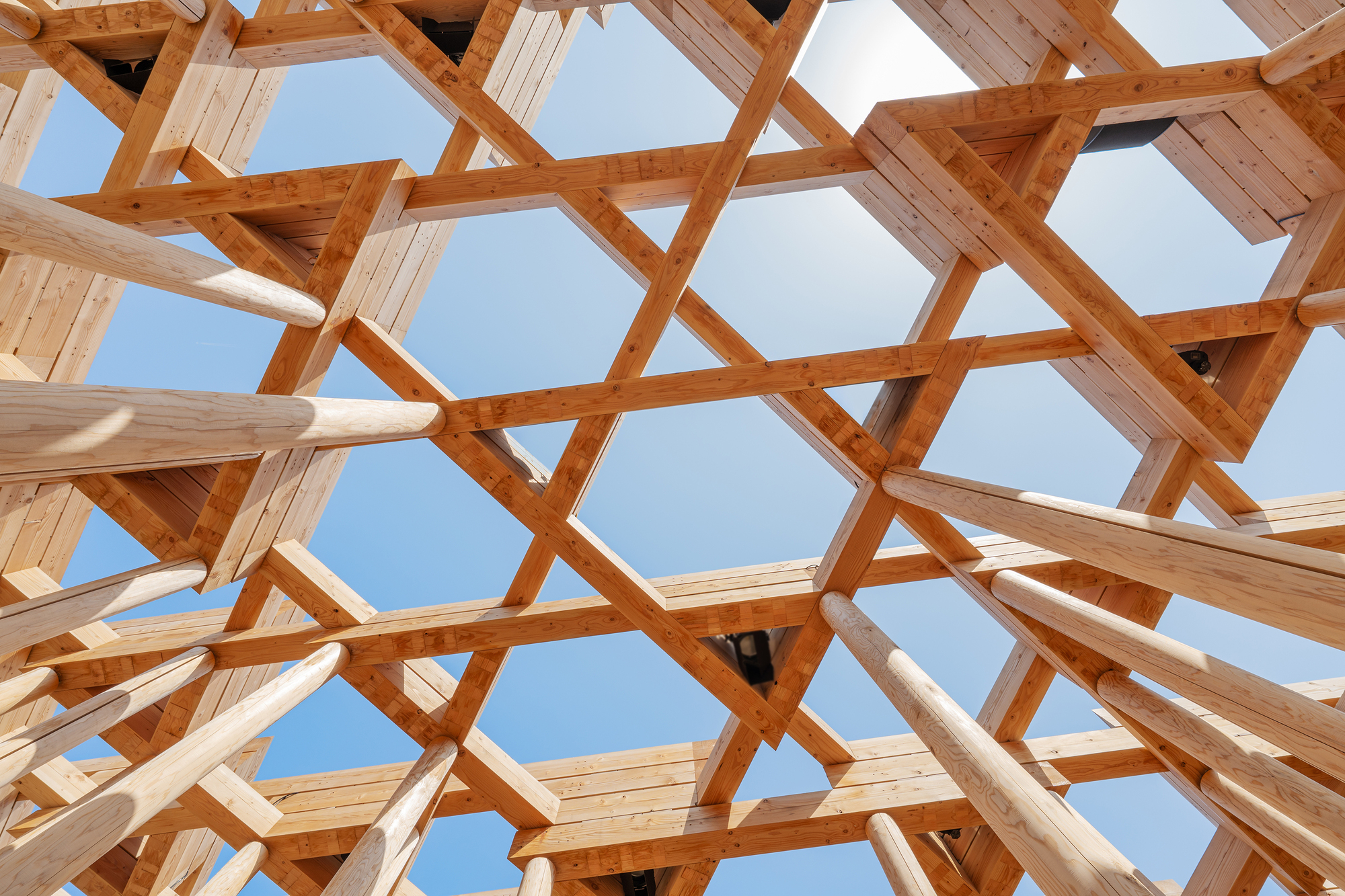 Upward view through a hexagonal timber lattice roof structure against clear sky