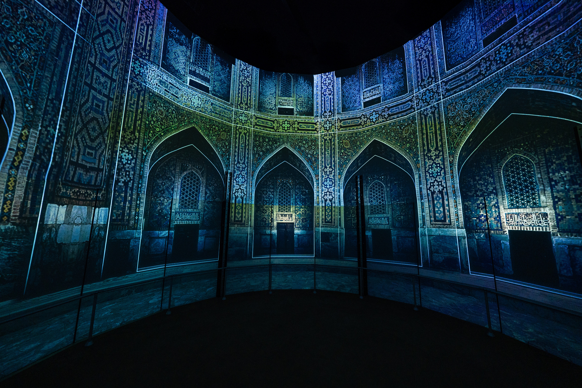 Interior courtyard with illuminated blue tilework and pointed arch alcoves reflected in a polished dark floor