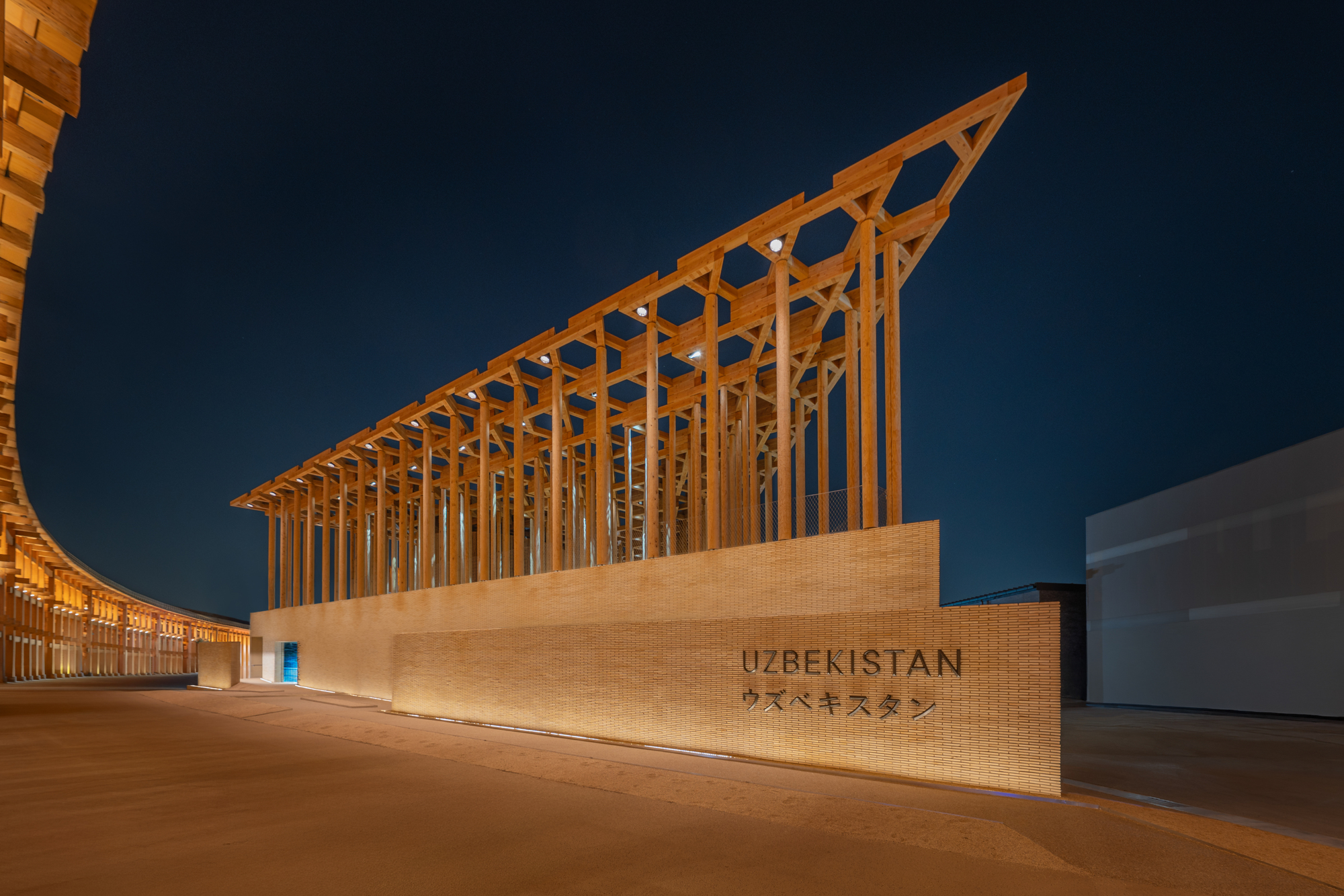 Timber canopy with angled slats rising above a sandstone wall at dusk