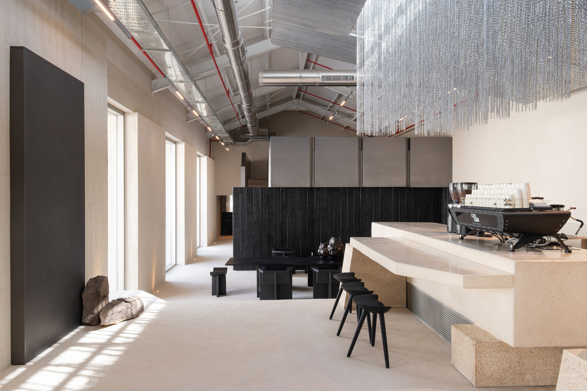 Coffee bar interior with charred timber volume, terrazzo counter, and suspended chain chandelier under exposed trusses