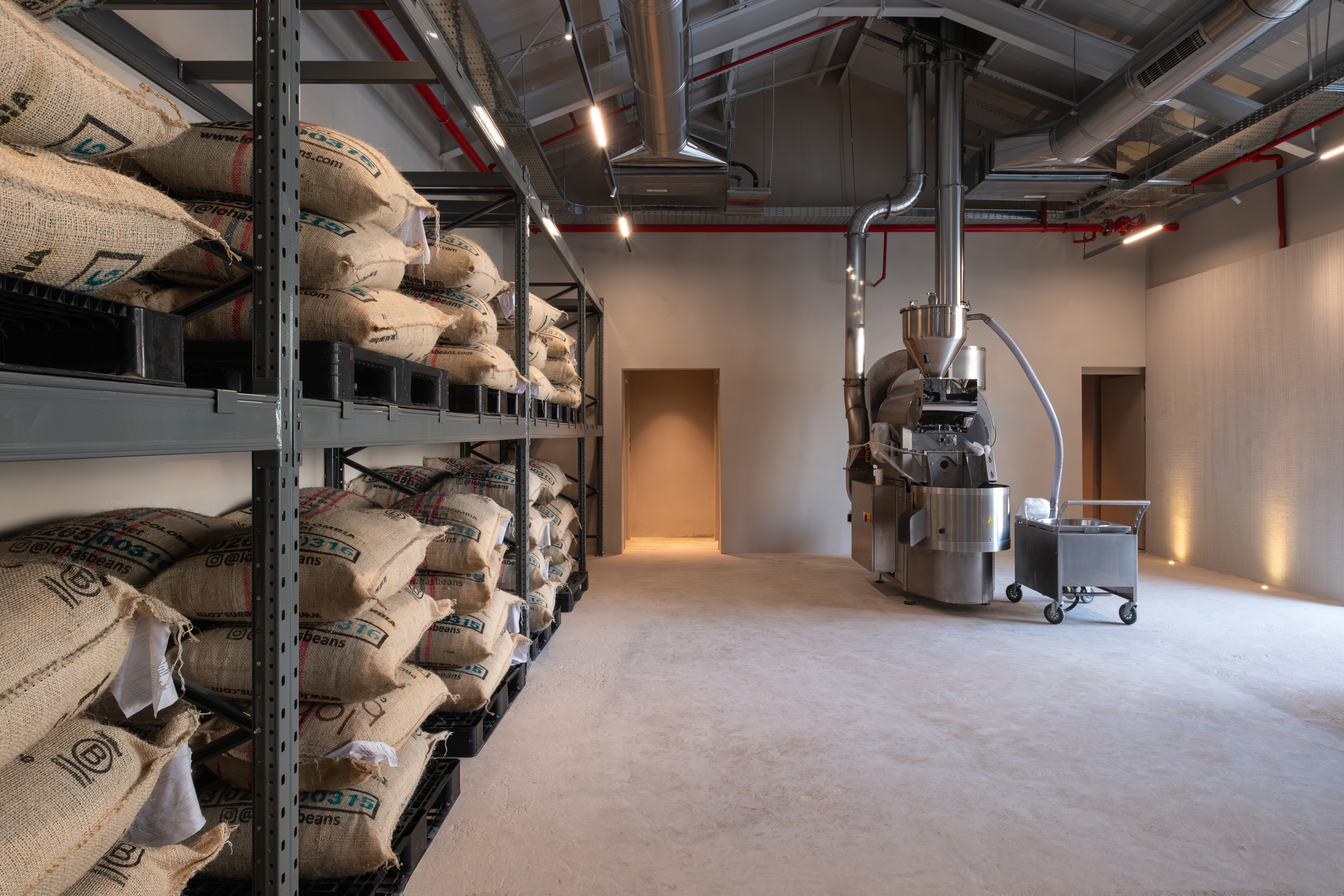 Coffee roastery interior with burlap sacks stacked on metal shelving and exposed mechanical ductwork overhead