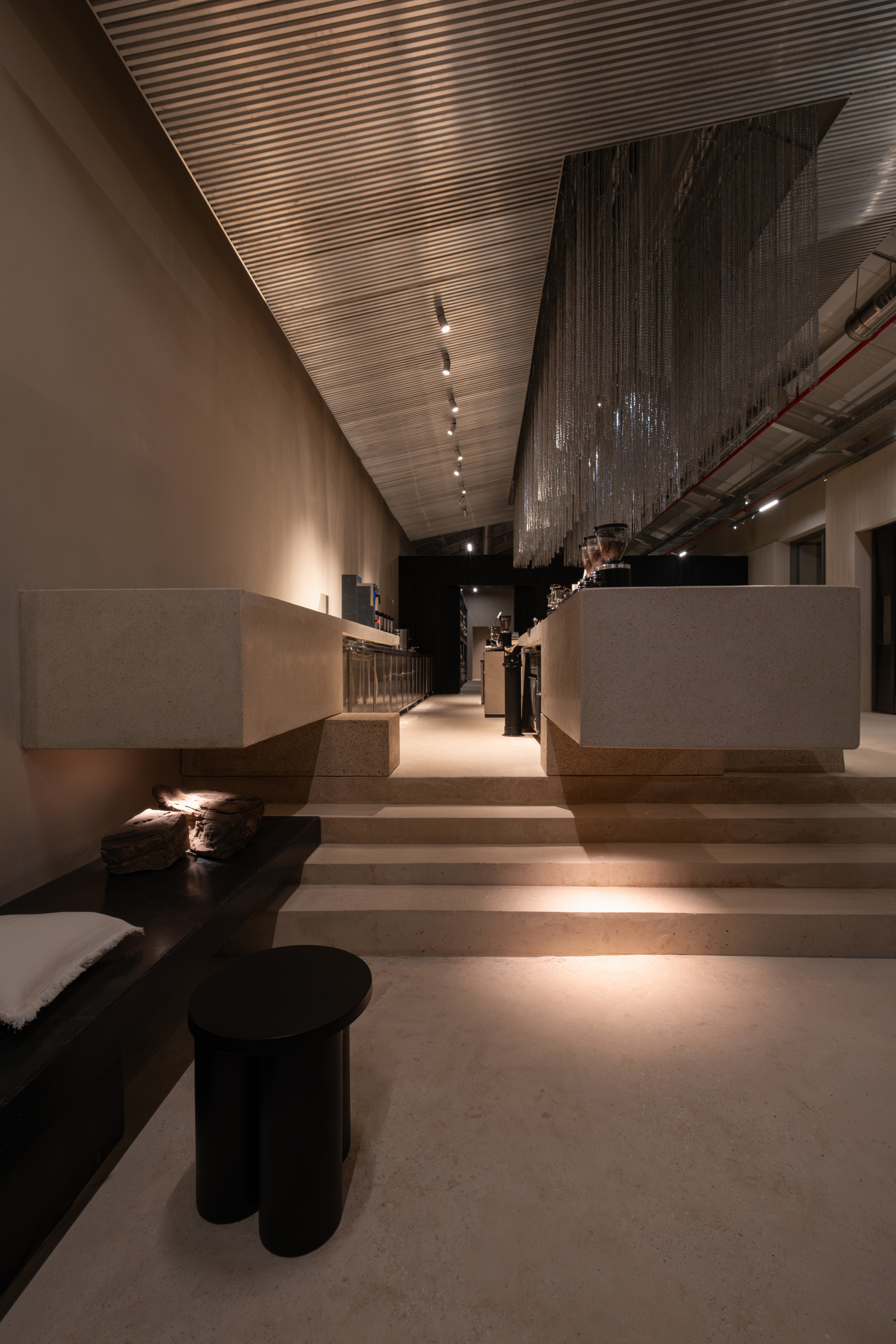 Stepped seating area with terrazzo platforms and slatted ceiling under ambient evening lighting