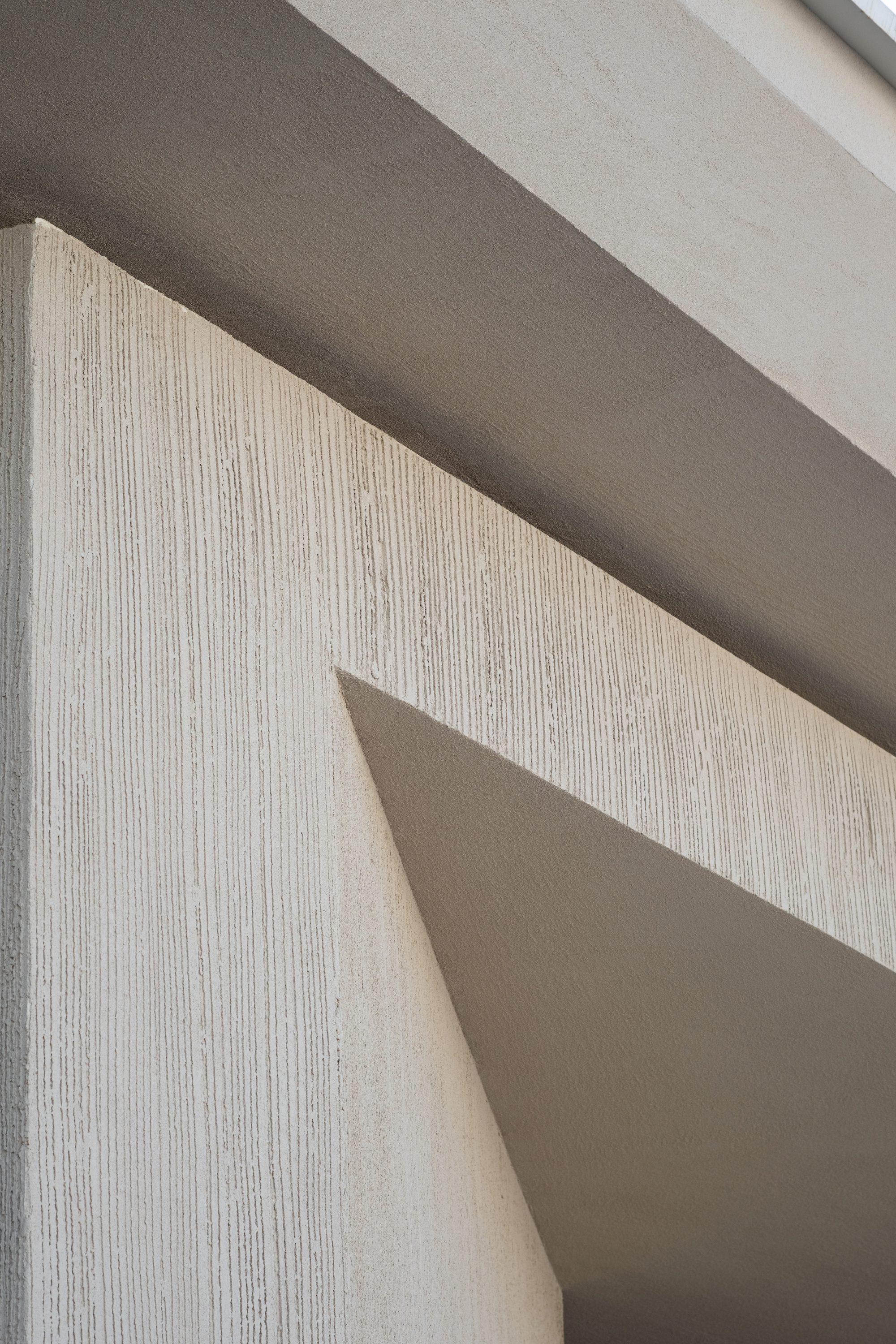 Close-up of vertically striated concrete wall meeting smooth soffit planes under natural daylight