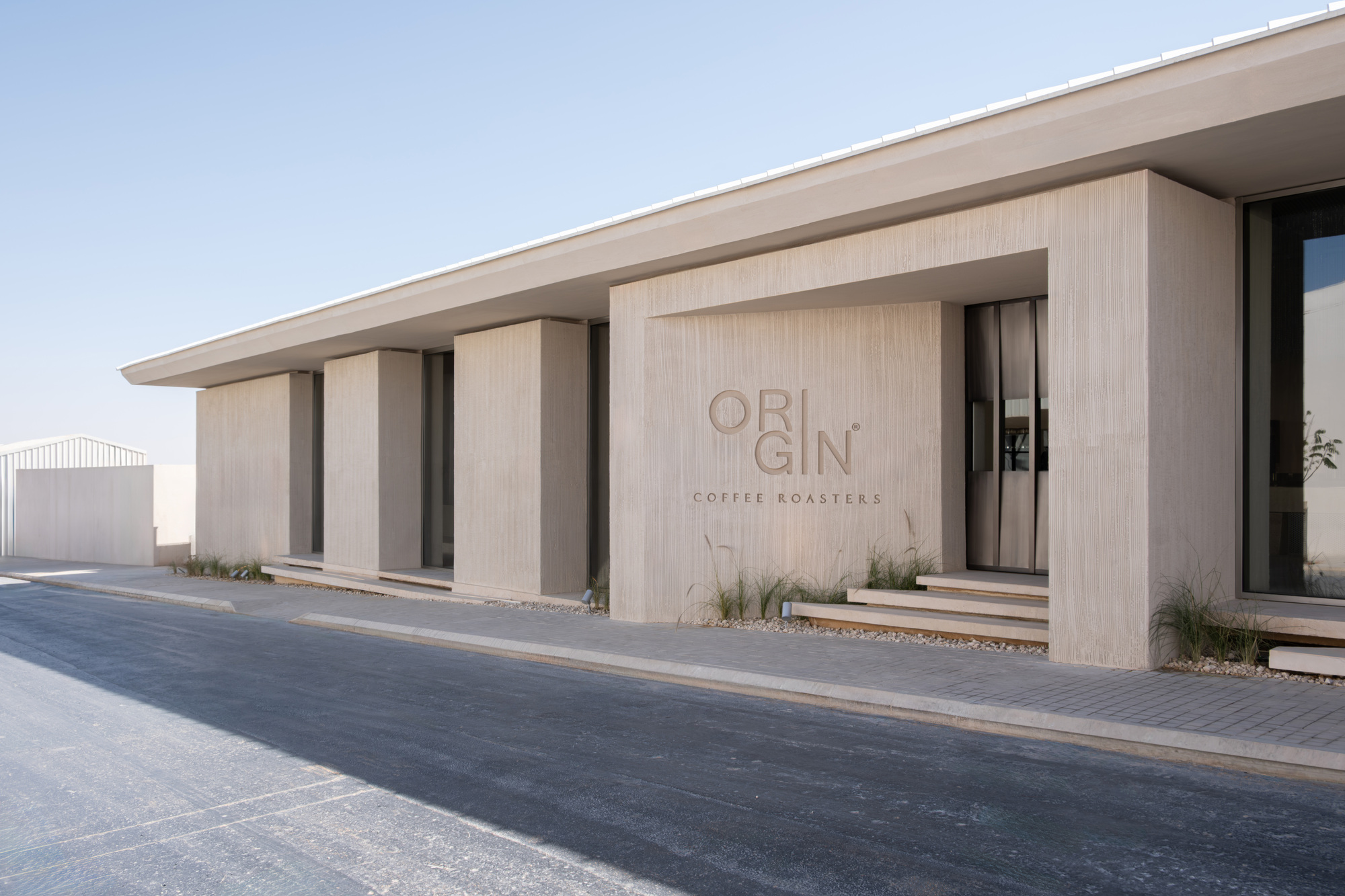 Ribbed concrete facade with recessed openings and flush-mounted signage under a clear desert sky