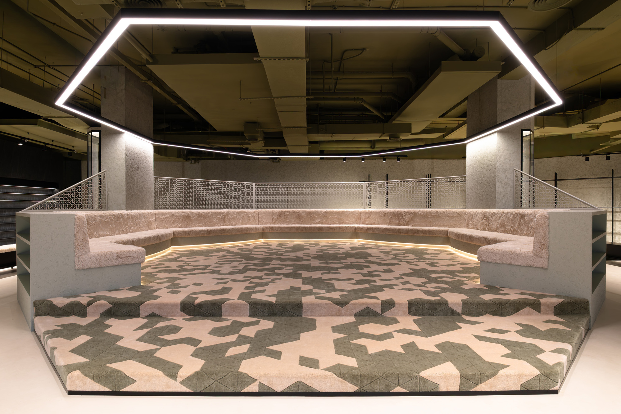 Sunken seating area with curved pink upholstered benches and geometric patterned floor under a pentagonal light fixture