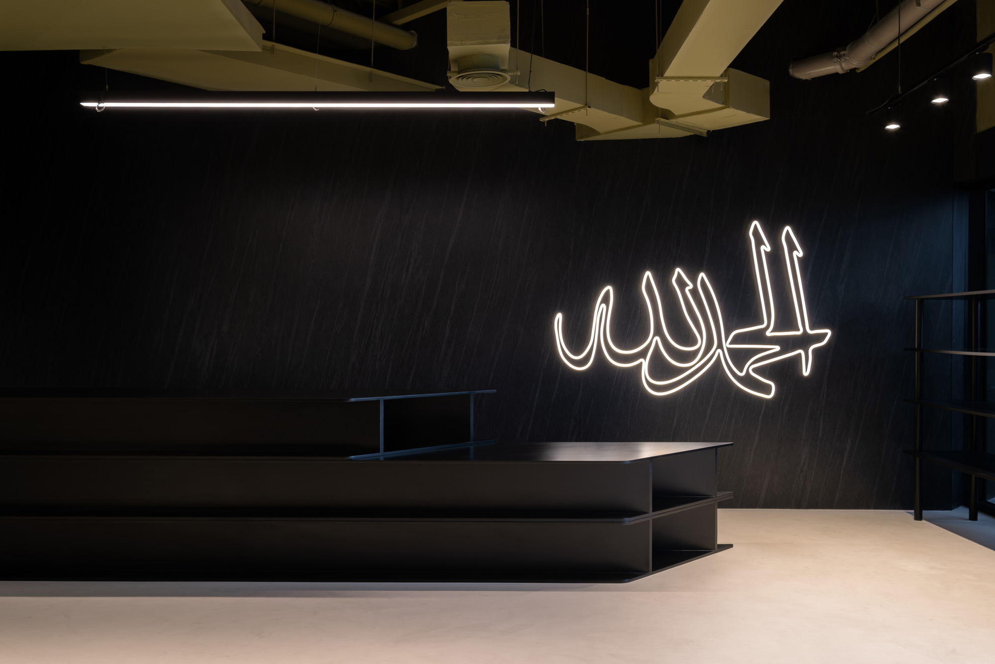 Dark feature wall with white neon Arabic calligraphy above low platform seating and polished concrete floor