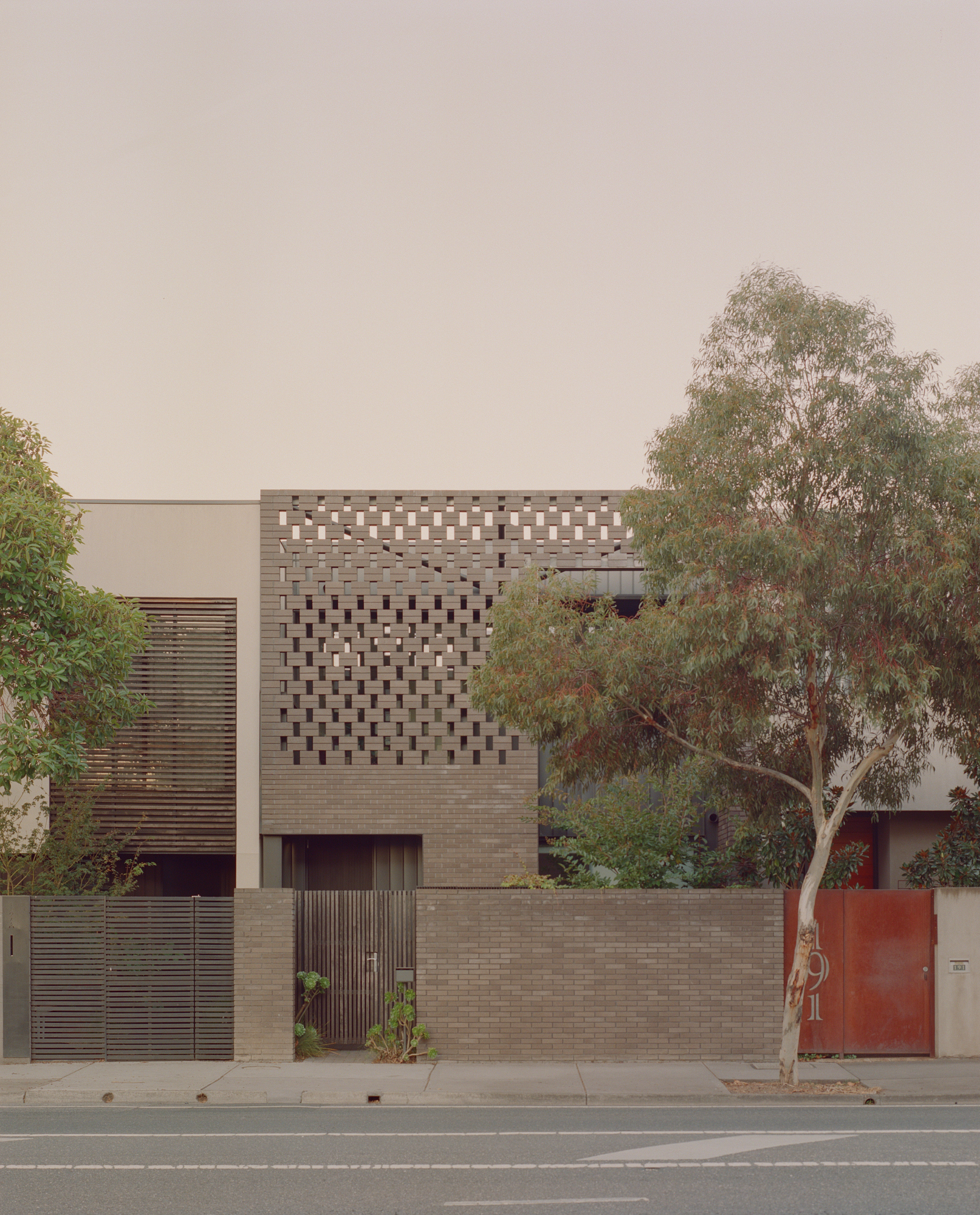 Street facade with perforated brick screen above a timber-slatted gate and planted boundary wall