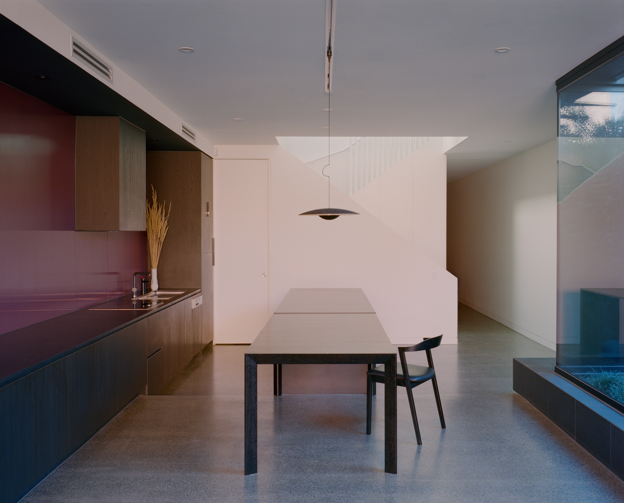 Minimal dining space with timber cabinetry, suspended pendant light and polished concrete floor