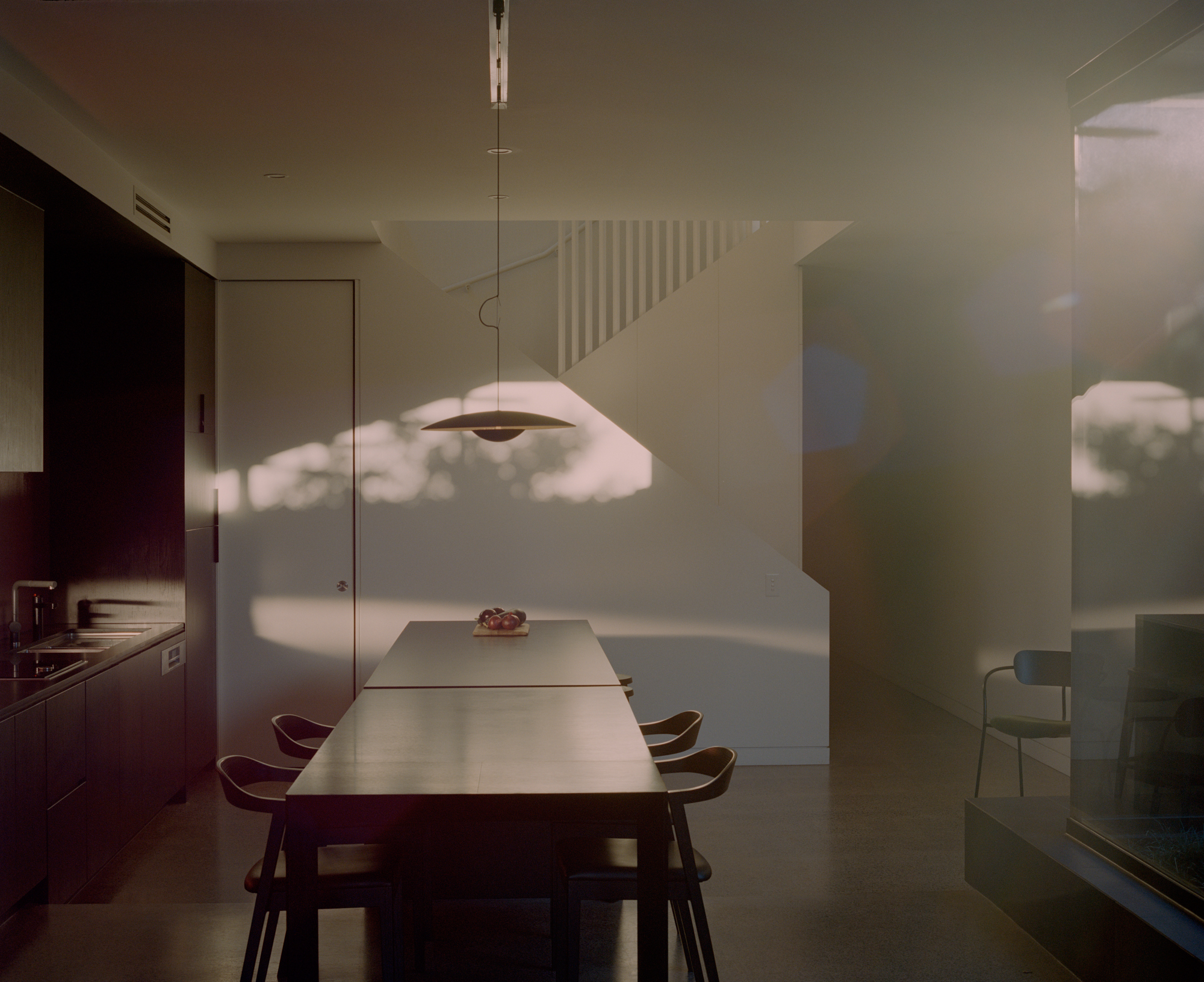 Dining space with suspended pendant lamp casting shadow patterns across white walls in afternoon light