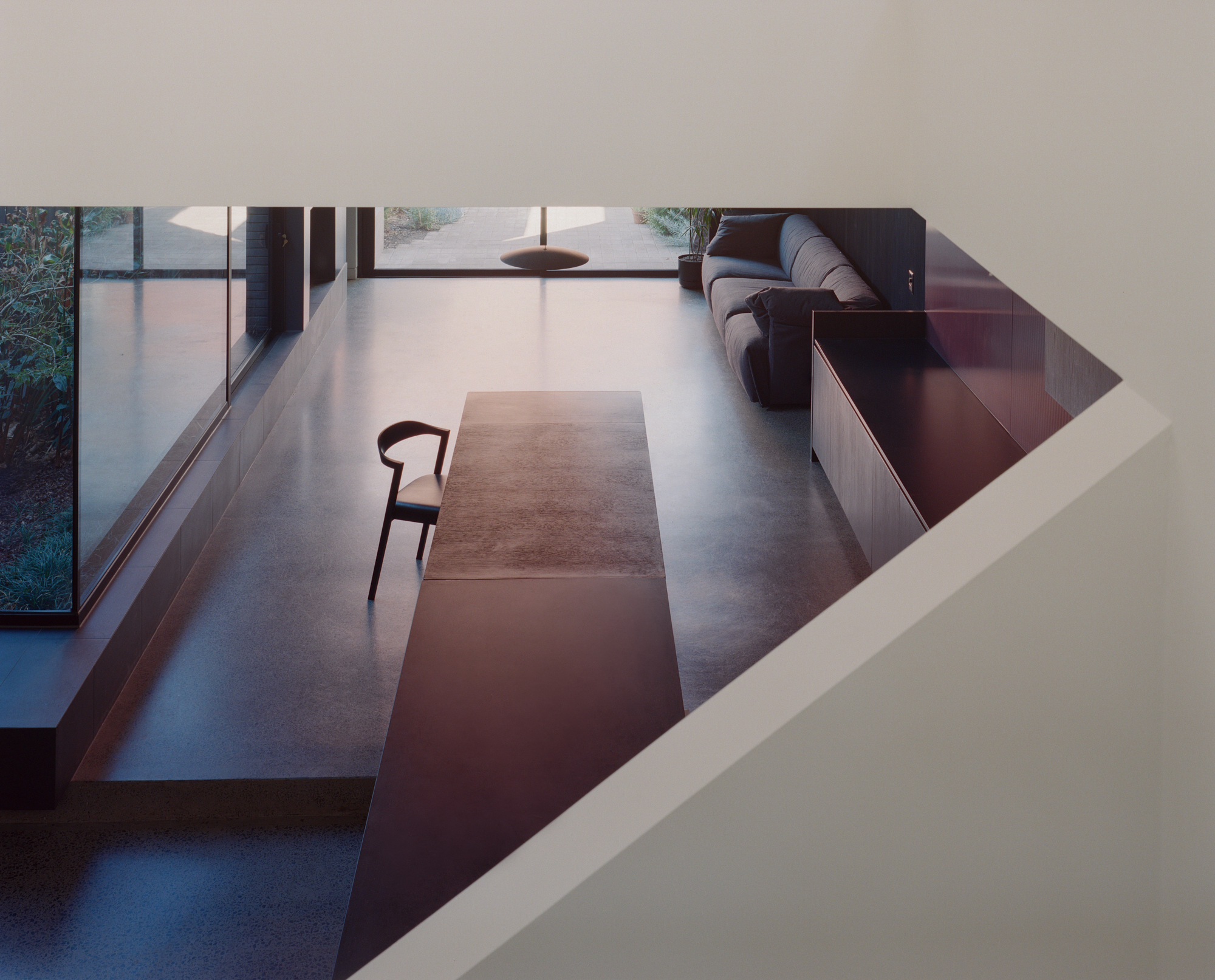 View down through ceiling aperture to lower level living space with polished concrete floor and low couch