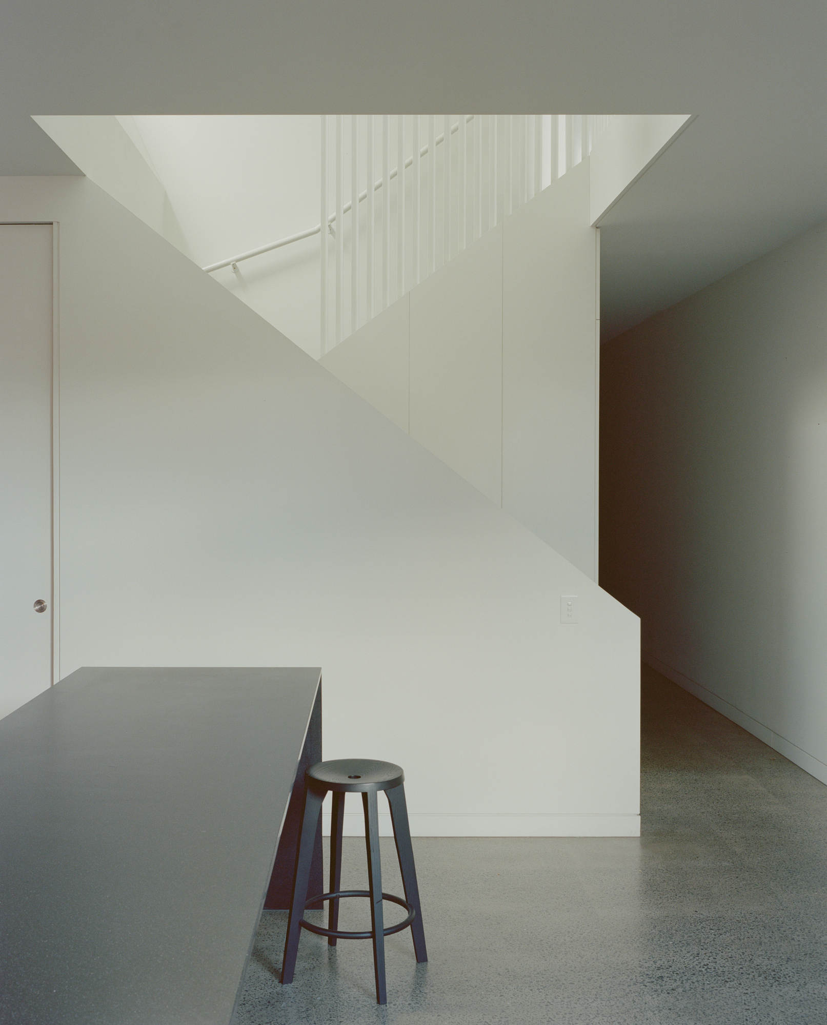 White staircase with vertical metal rods as railing rising beside a grey kitchen island with stool