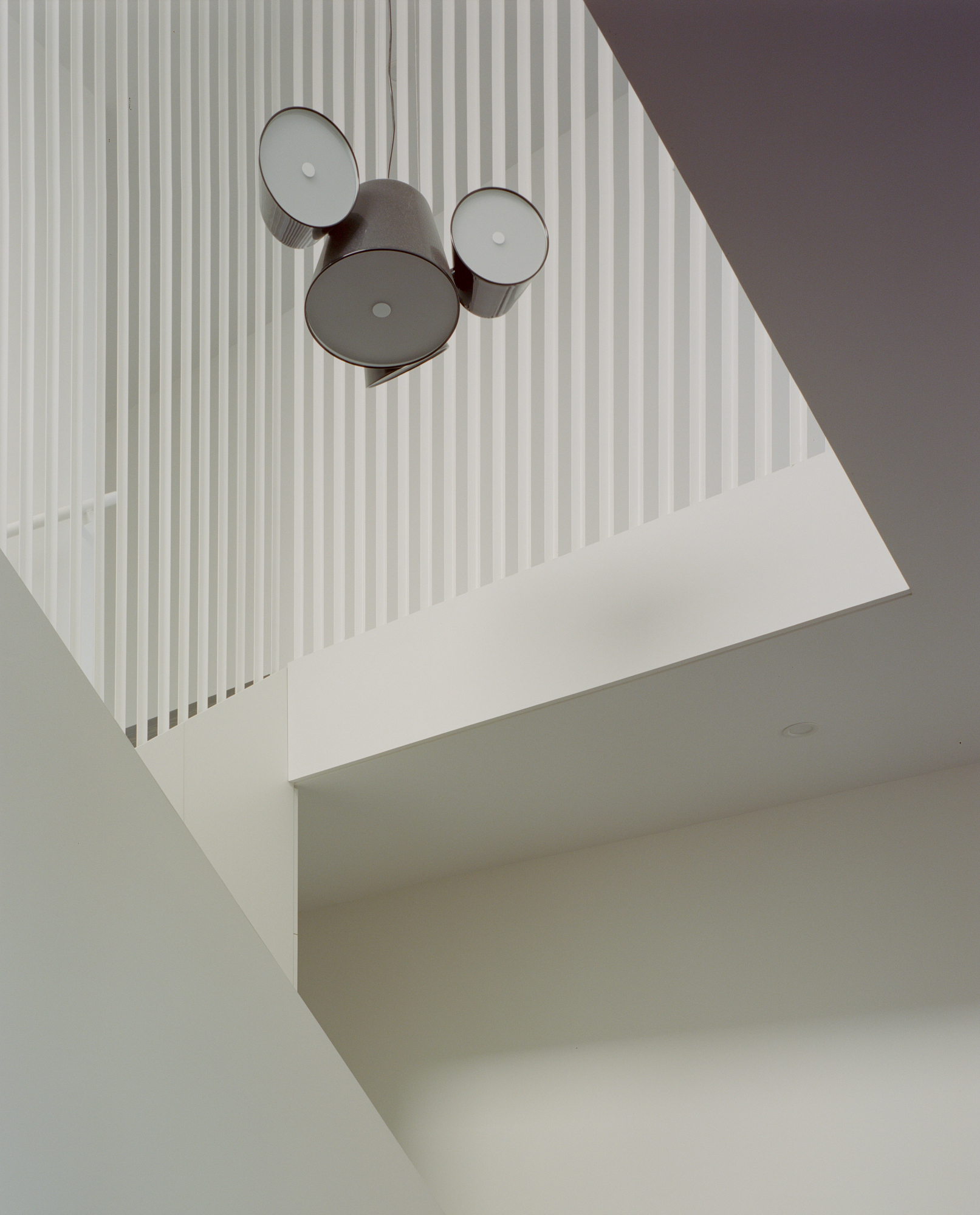 Looking up through stairwell void at cluster of three drum pendant lights against vertical rod railings