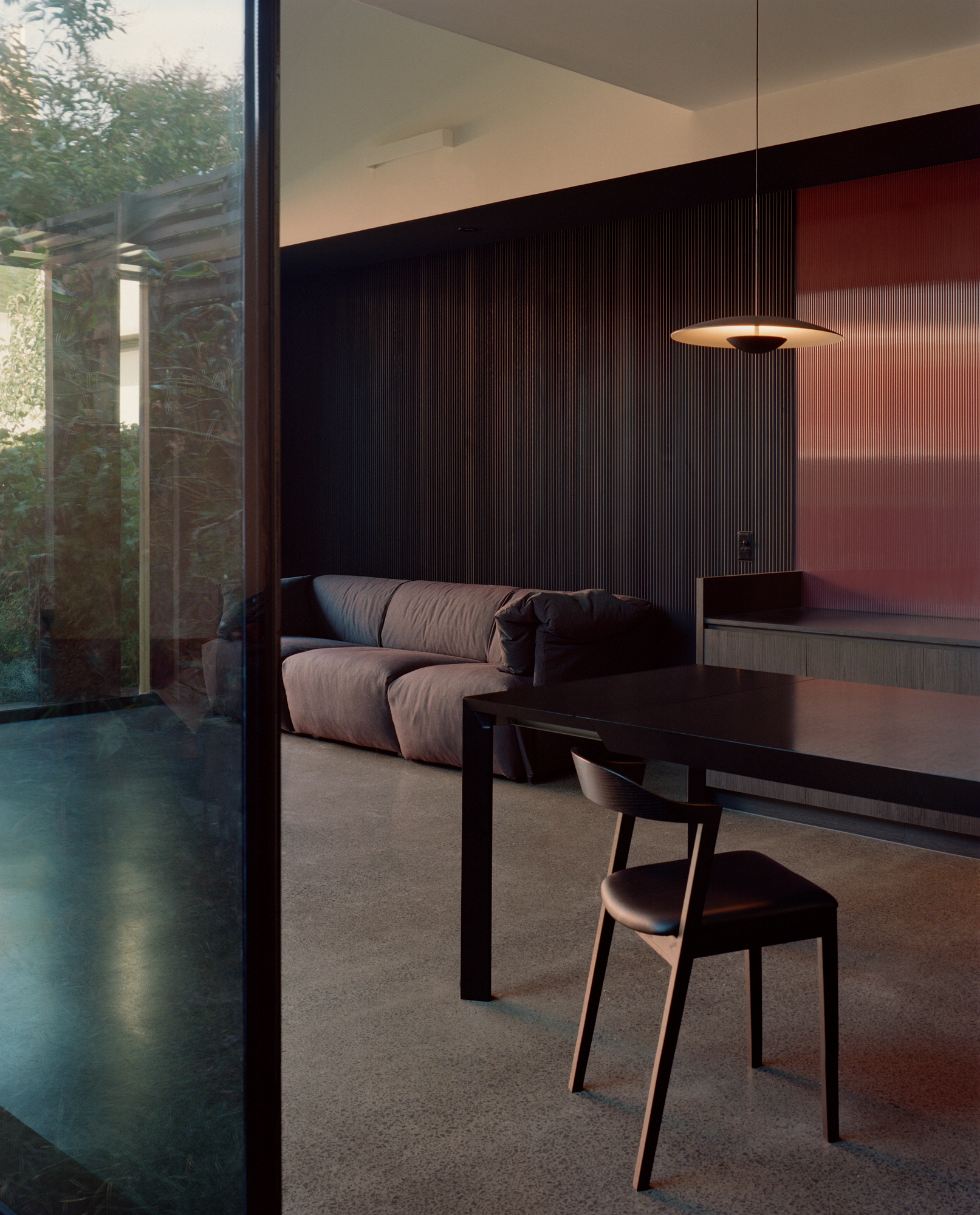 Living area with fluted timber wall and glazed courtyard door opening to planted exterior at twilight