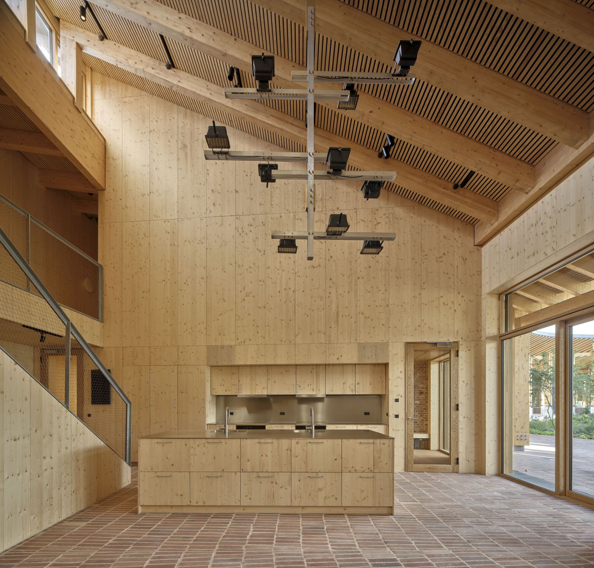 Interior foyer with cross-laminated timber walls, slatted ceiling, brick floor and suspended lighting fixtures