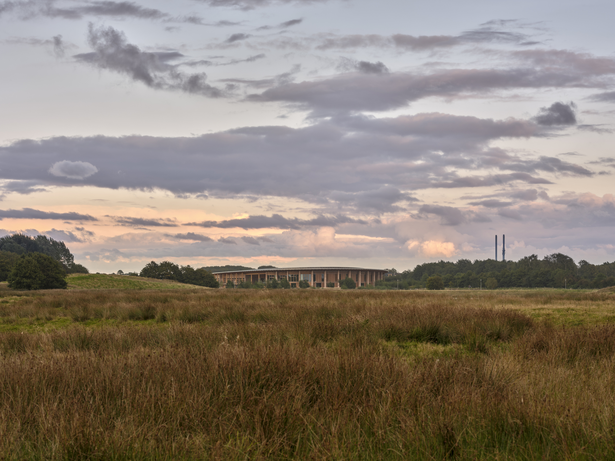 Distant view of the oval building across a wild meadow at dusk