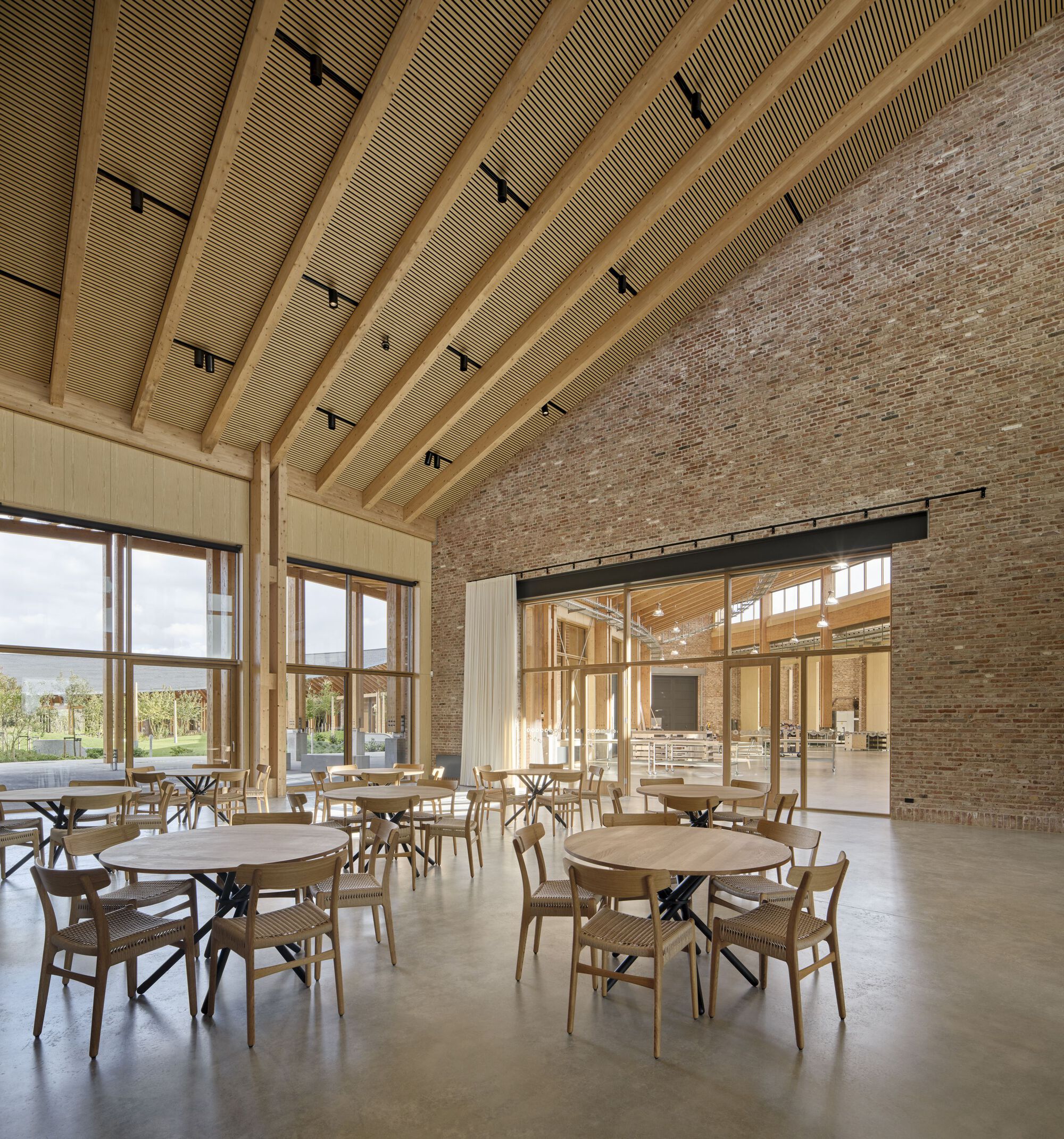 Dining hall interior with curved timber ceiling, brick wall and large windows overlooking the landscape