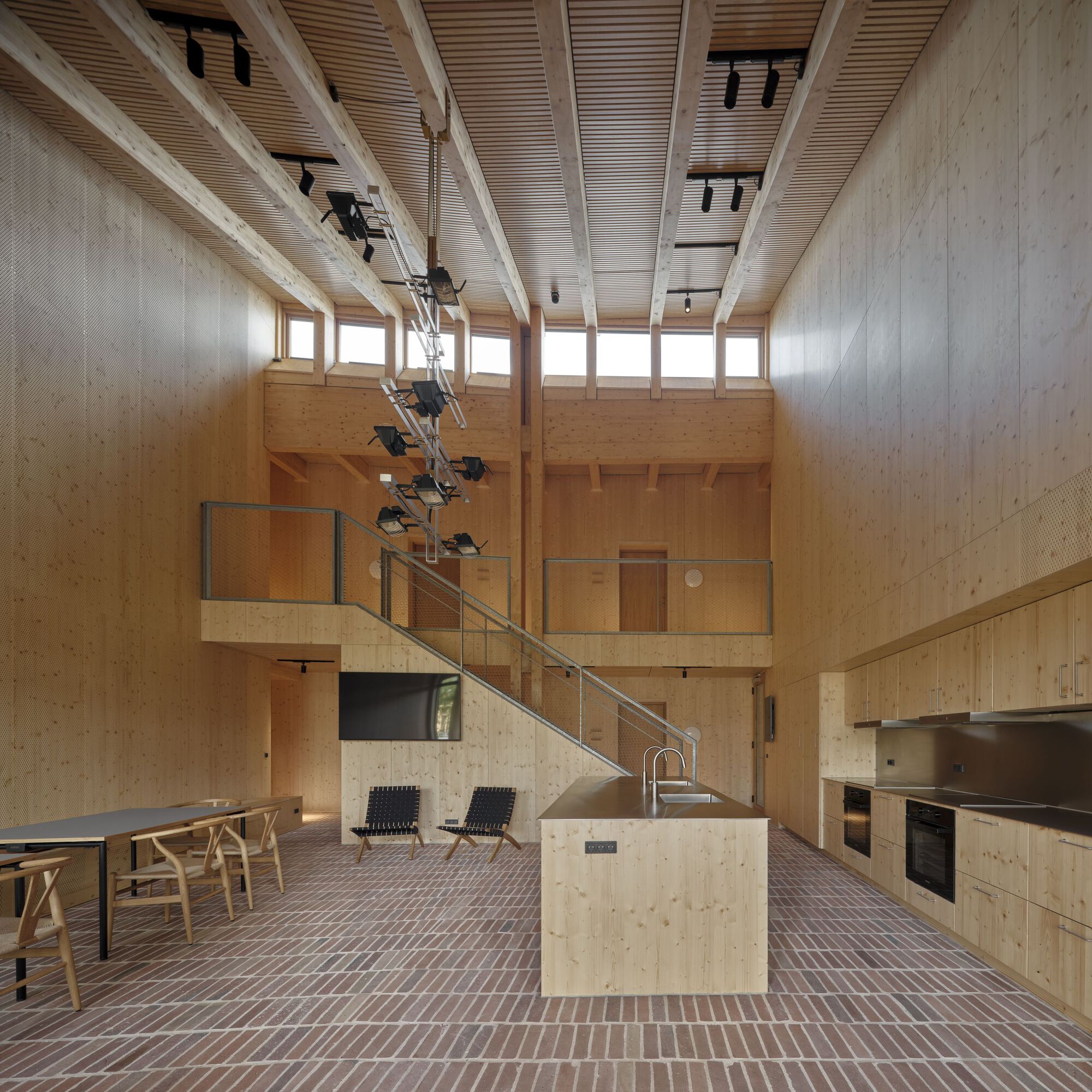 Double-height kitchen space with timber walls, mezzanine staircase and brick tile flooring throughout