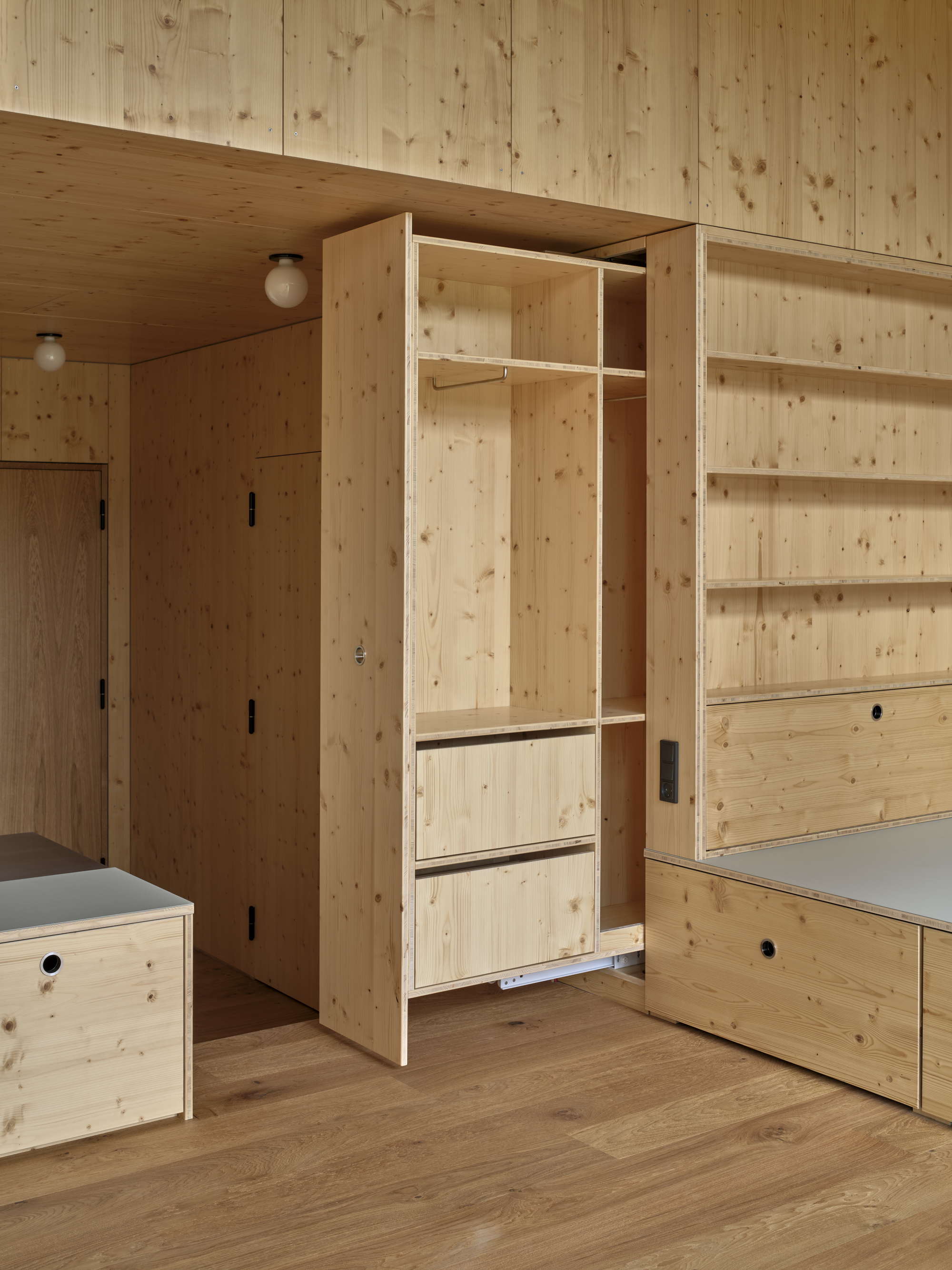 Open plywood wardrobe with hanging rail and drawers beside integrated shelving along the wall