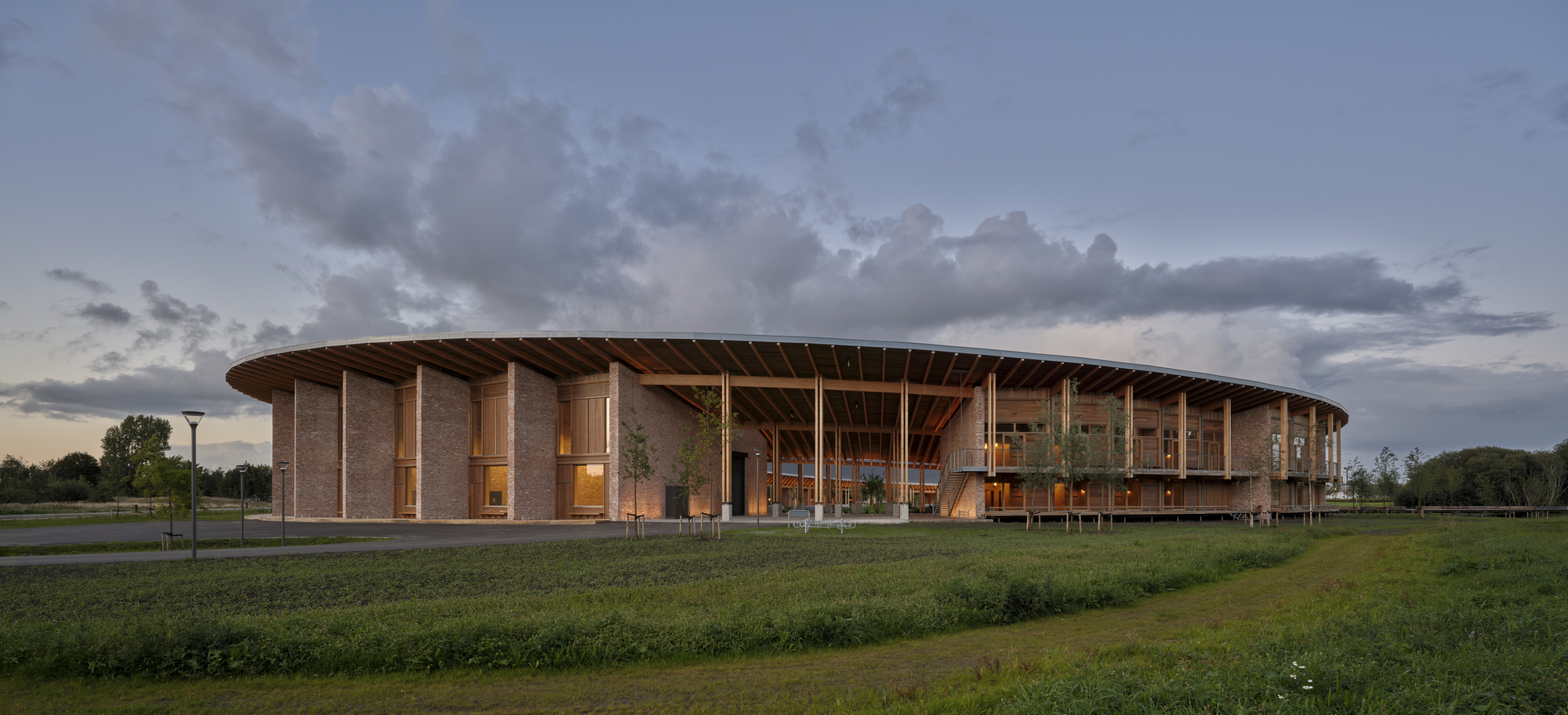 Circular colonnade with timber roof structure and brick piers across an open field at twilight