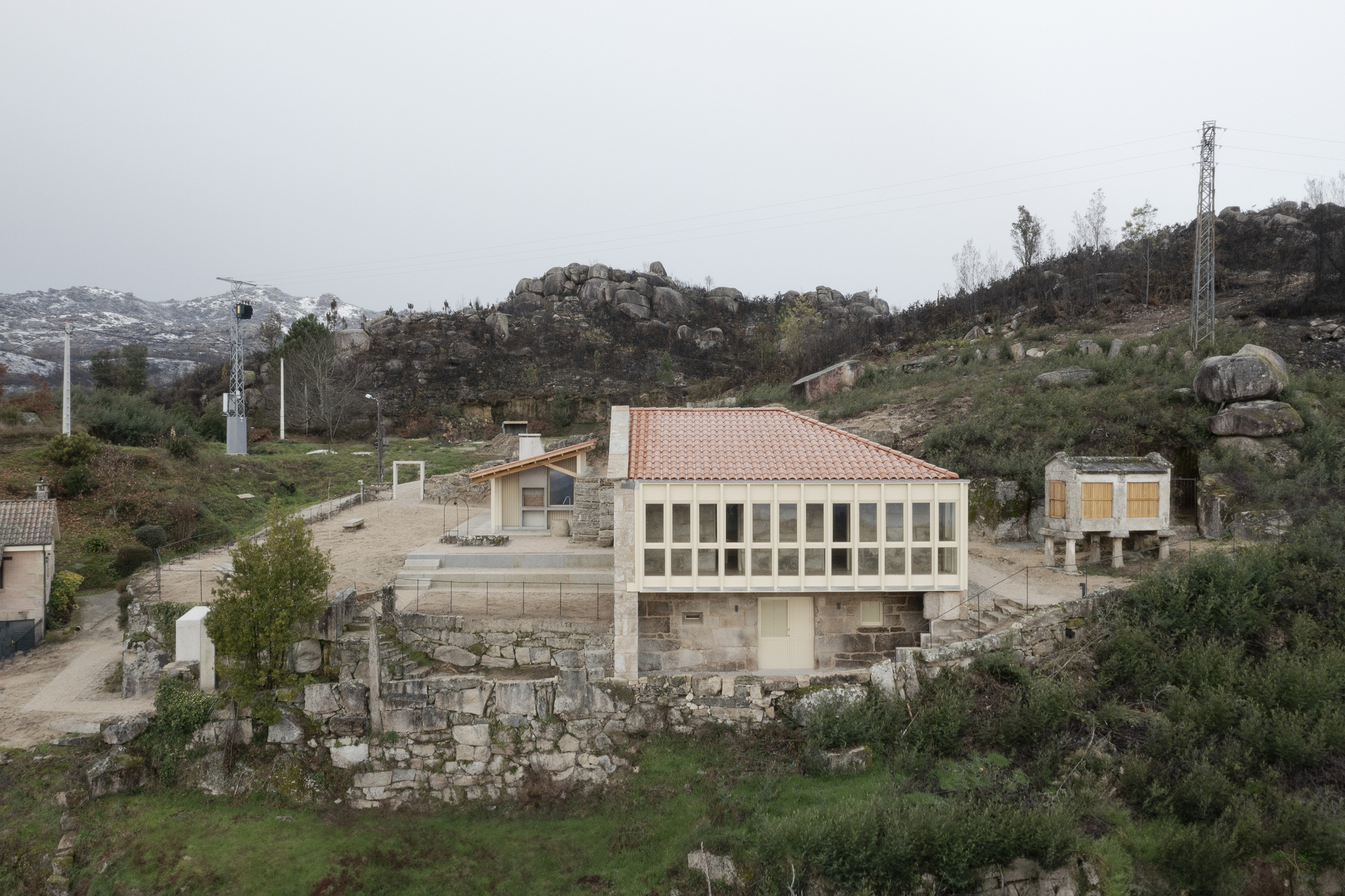Cluster of stone and timber structures with terracotta roofs on a rocky hillside in overcast weather