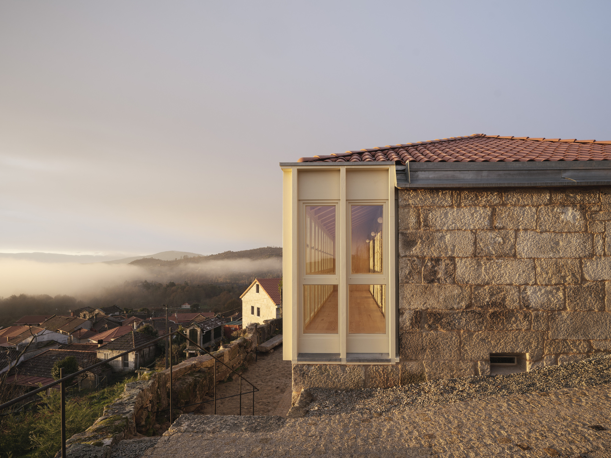 Corner junction where pale timber extension meets granite wall under terracotta tiles at dusk with valley fog
