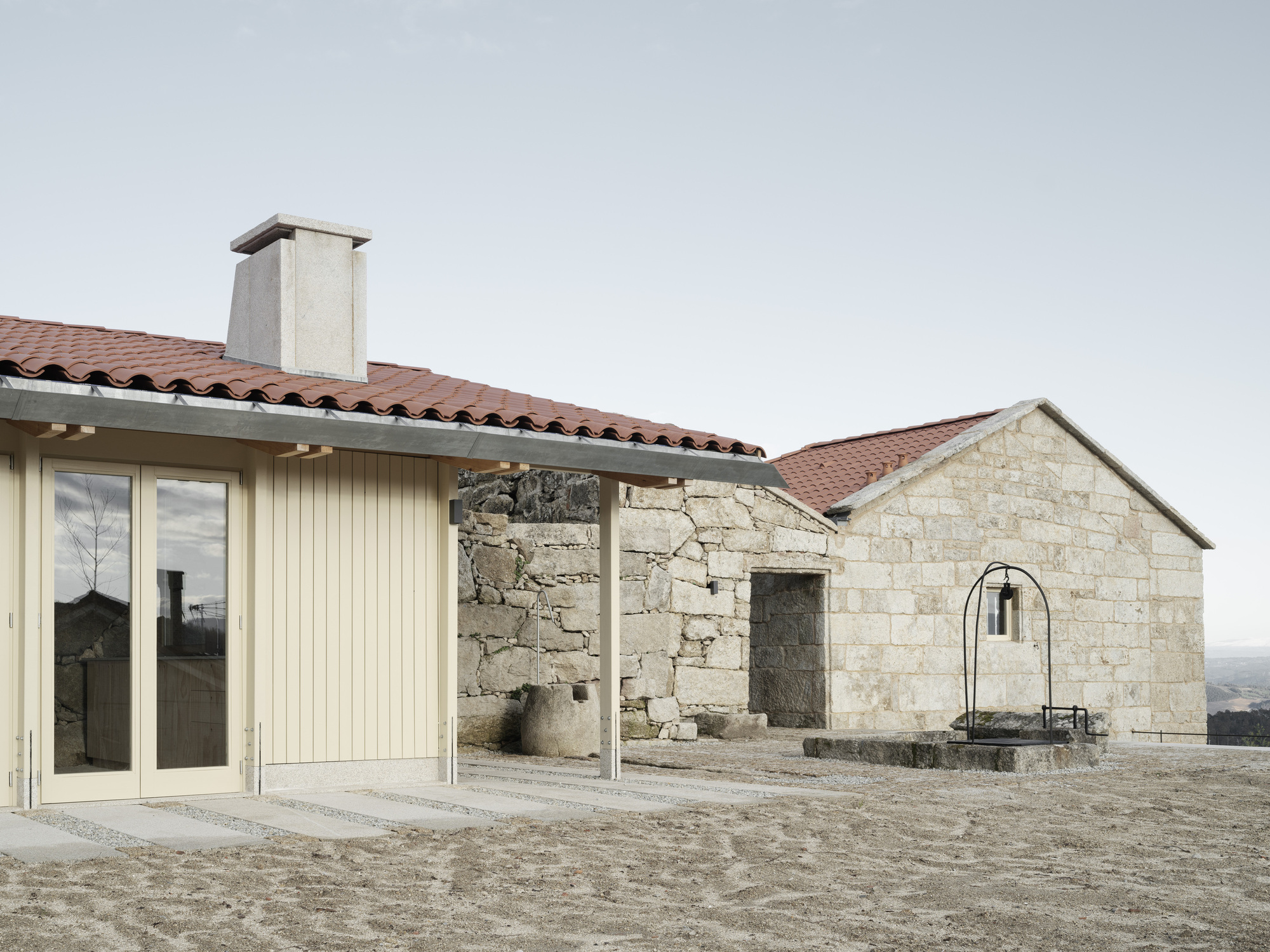 New timber-clad volume beside weathered granite ruin with arched doorway under cloudy sky