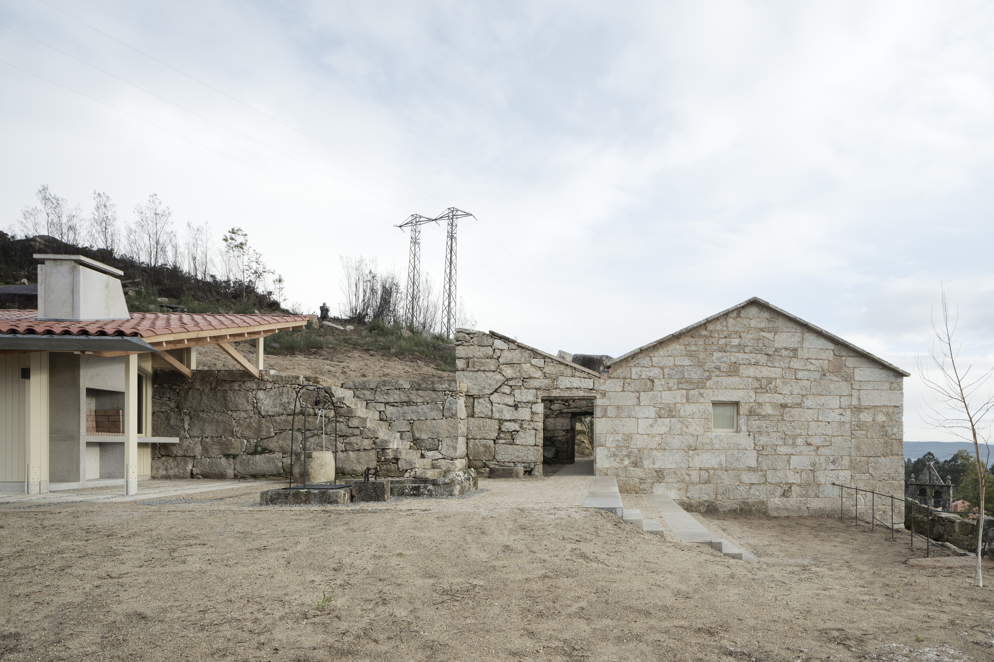Gravel courtyard with stone barn ruins and timber-framed pavilion under overcast skies