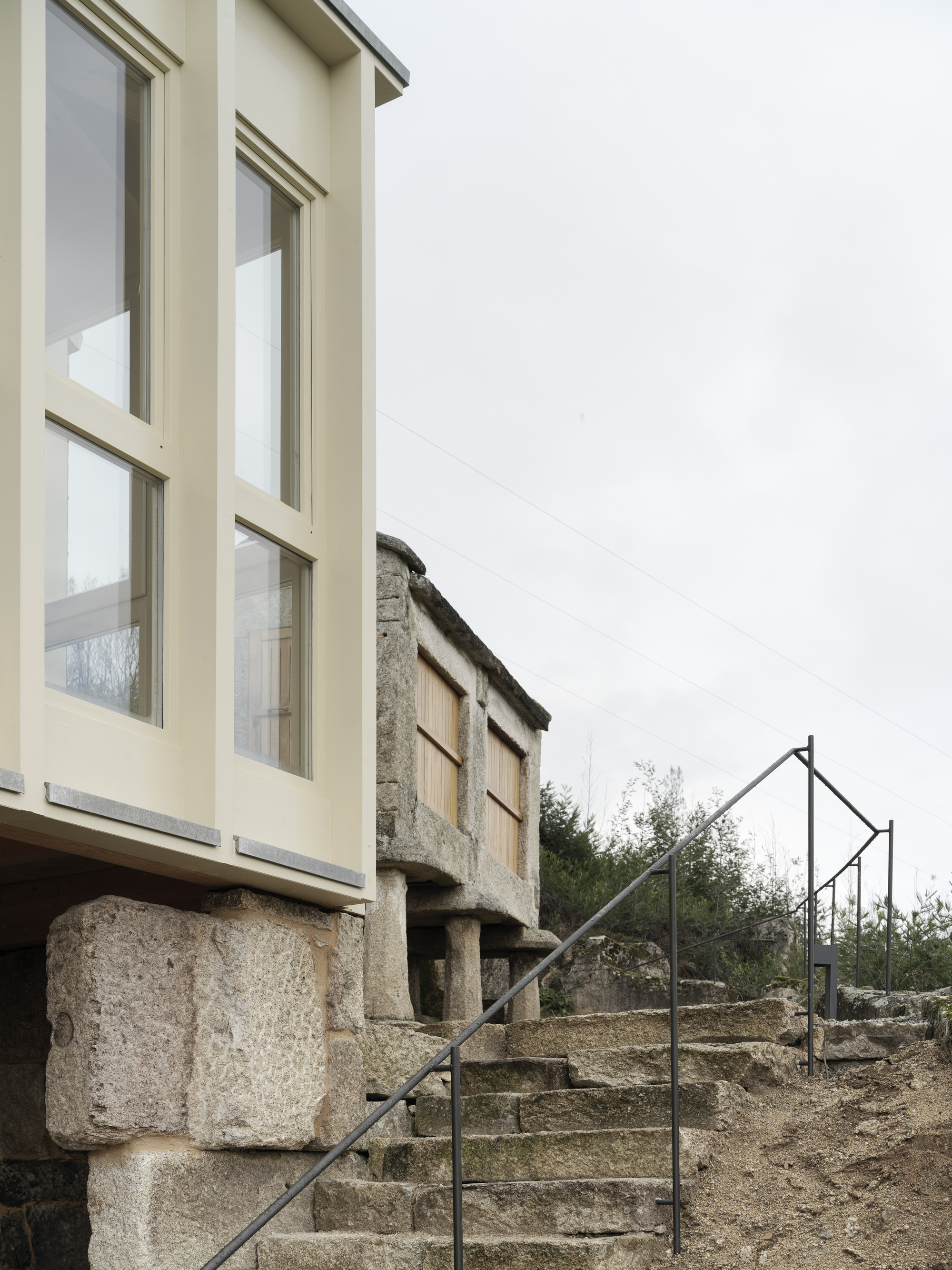 Stone staircase with minimal steel railing ascending beneath cantilevered facade volume