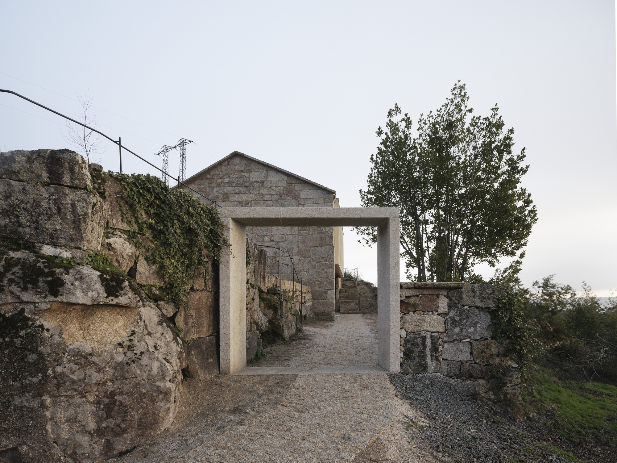 Concrete portal frame opening onto gravel path between weathered stone walls