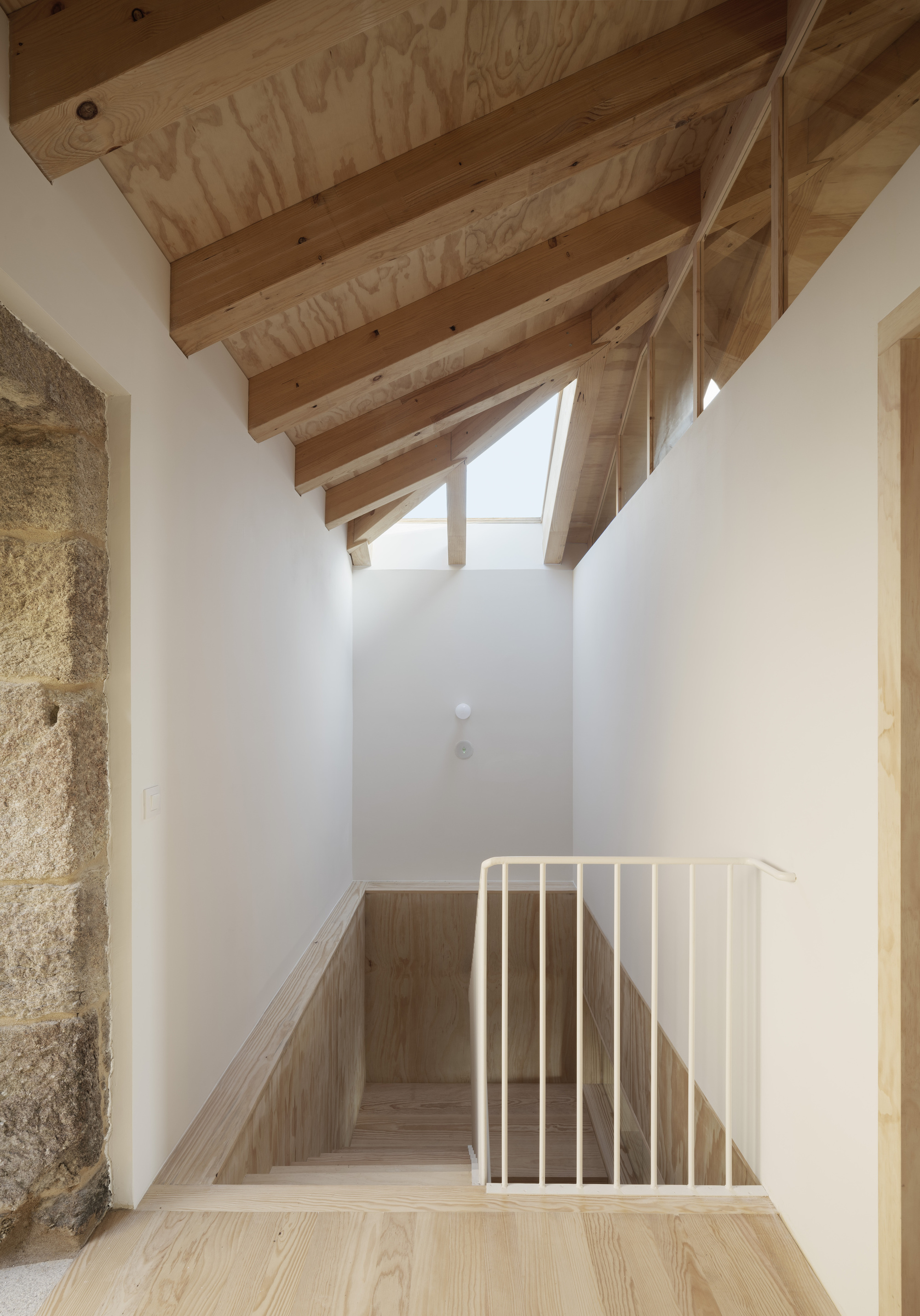 Interior staircase with exposed timber rafters and skylight illuminating white walls