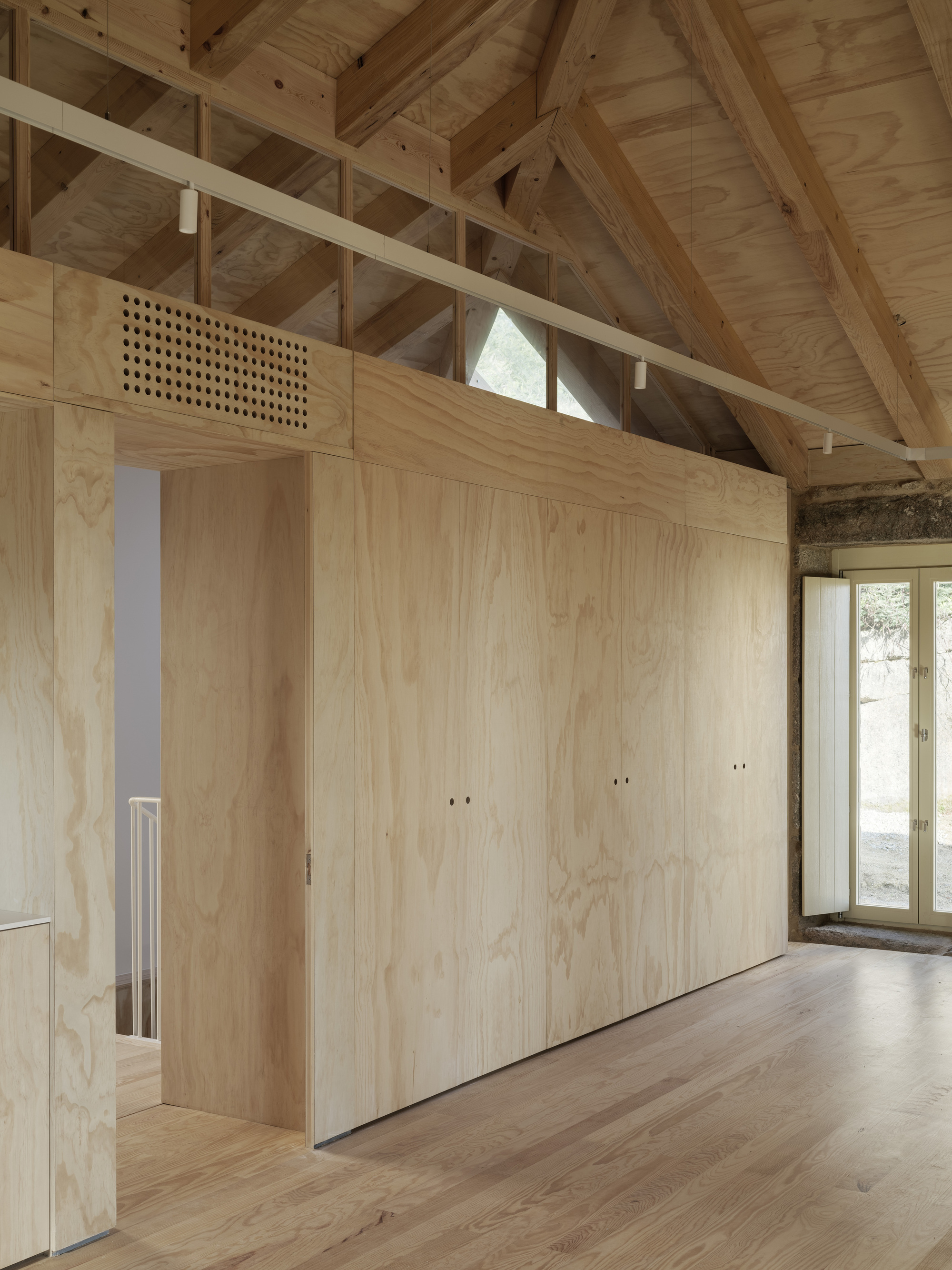 Plywood partition wall with integrated door and perforated ventilation grill beneath exposed timber roof structure