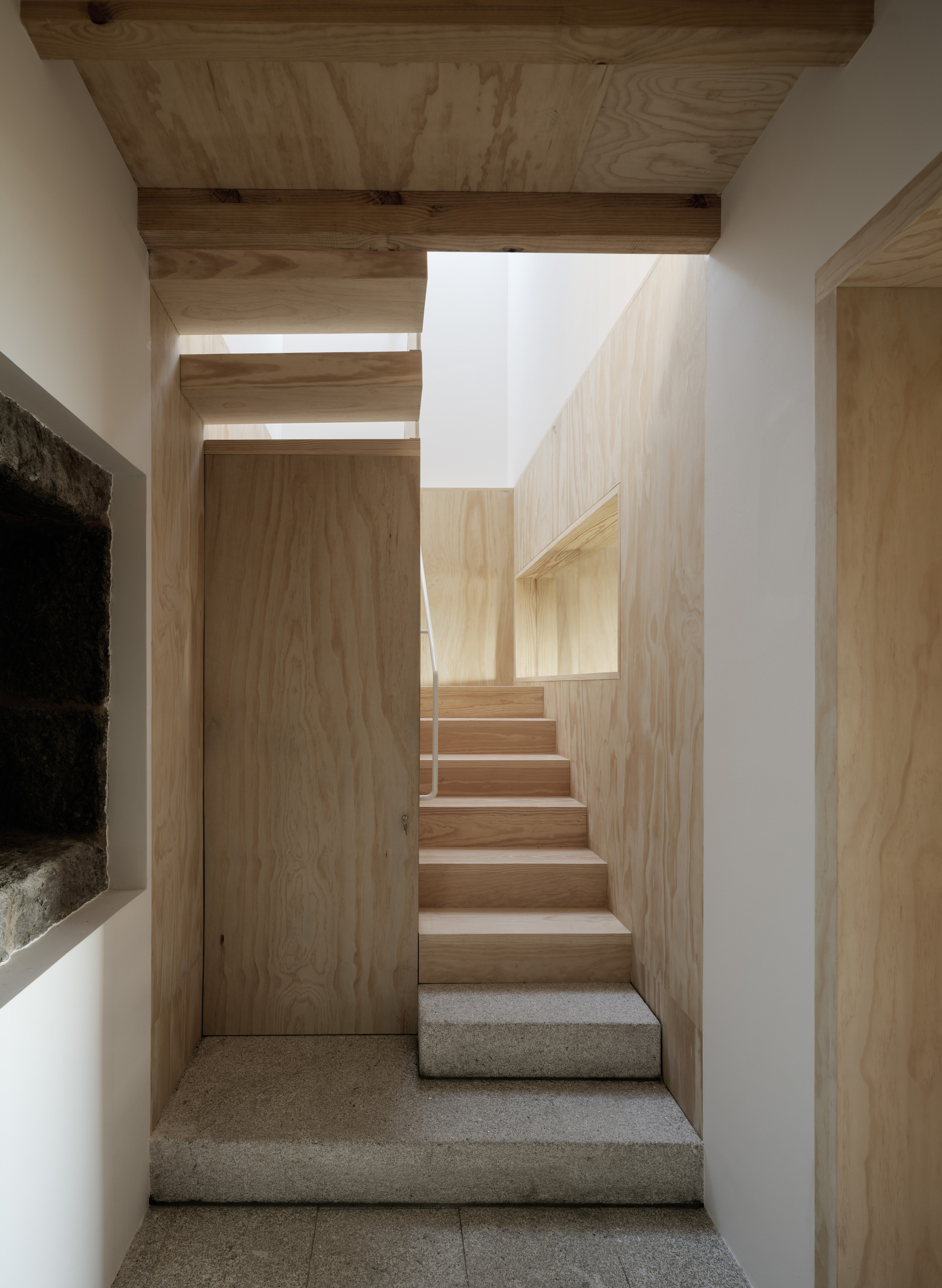 Timber and concrete staircase ascending through white plaster walls with daylight filtering from above