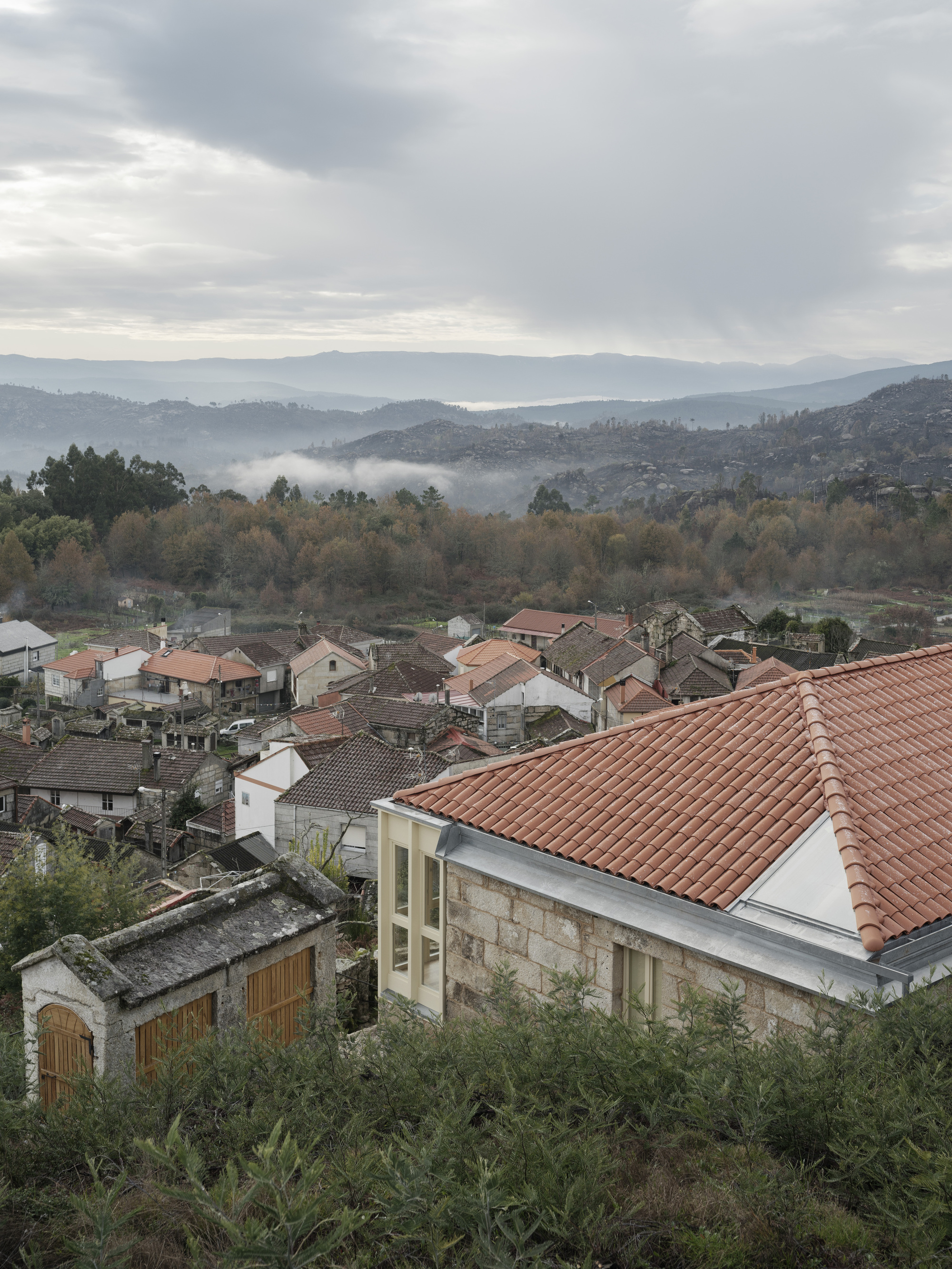 Terracotta roof among village houses with forested hills and low clouds in the distance