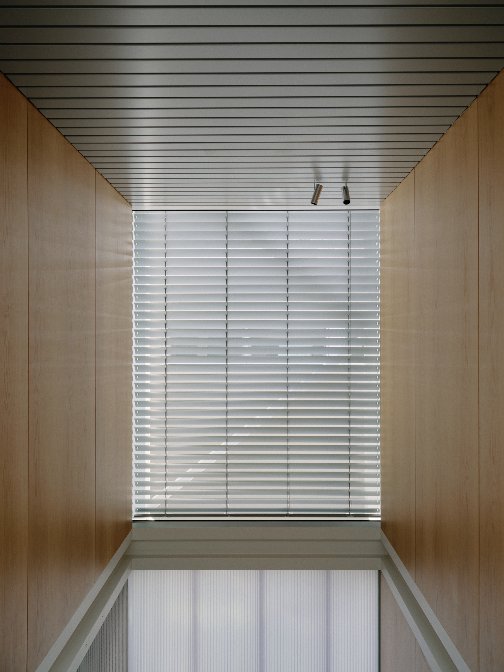 Wood-lined corridor with slatted metal ceiling and horizontal louvered window at end